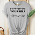Gray t-shirt with text 'Don't torture yourself, that's my job' on a hanger.