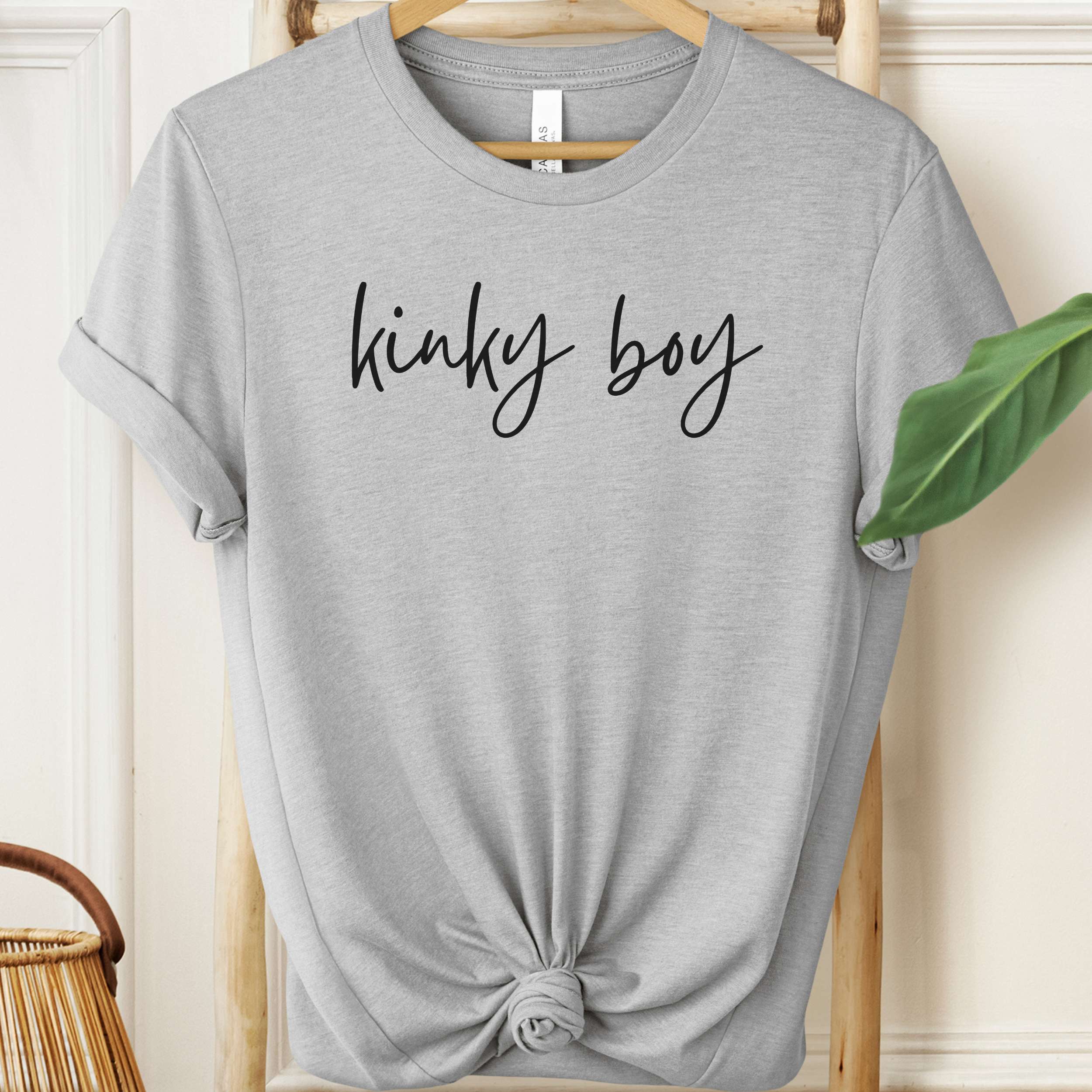 Gray t-shirt with 'kinky boy' text on a hanger against a neutral background