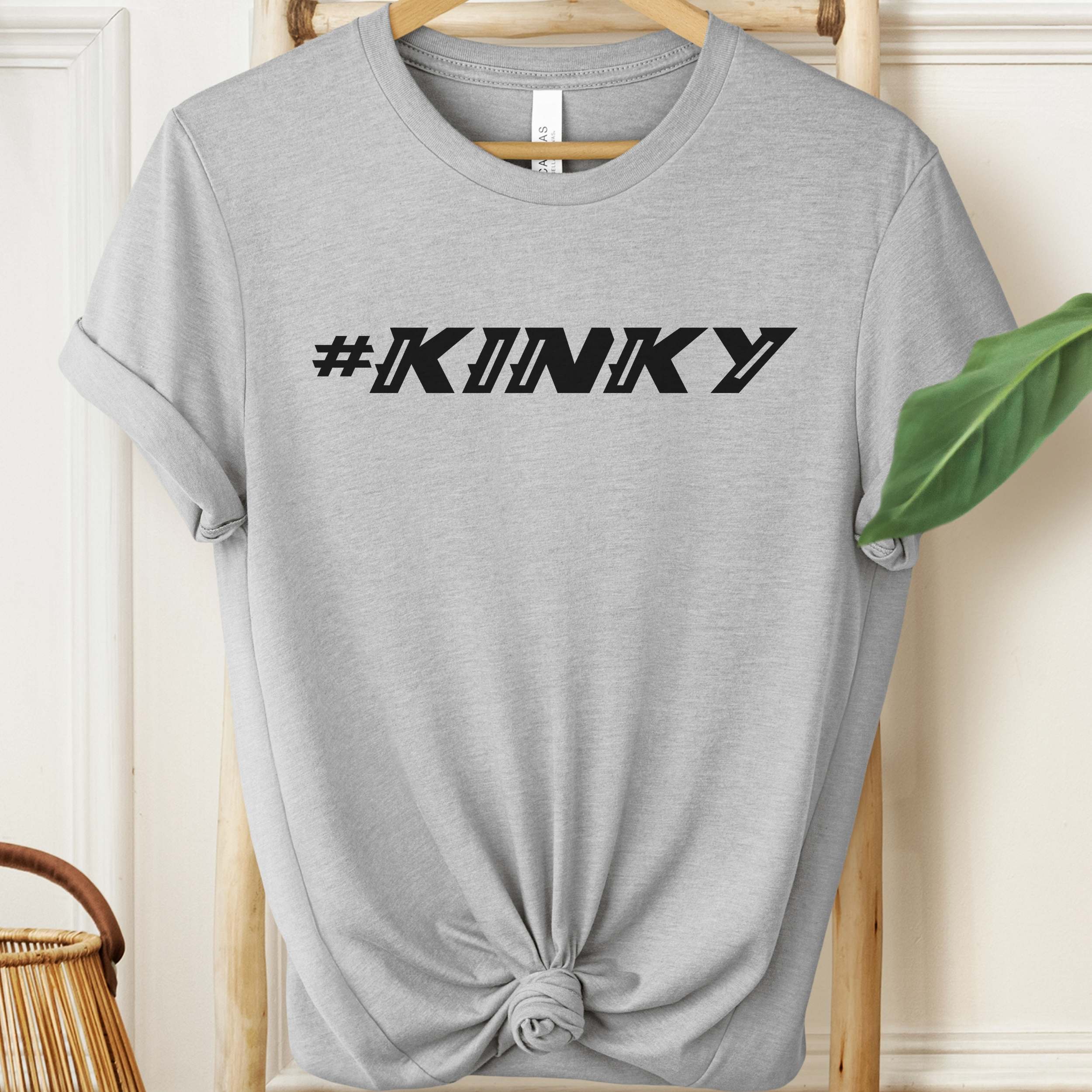 Gray t-shirt with '#KINKY' text on a hanger against a neutral background