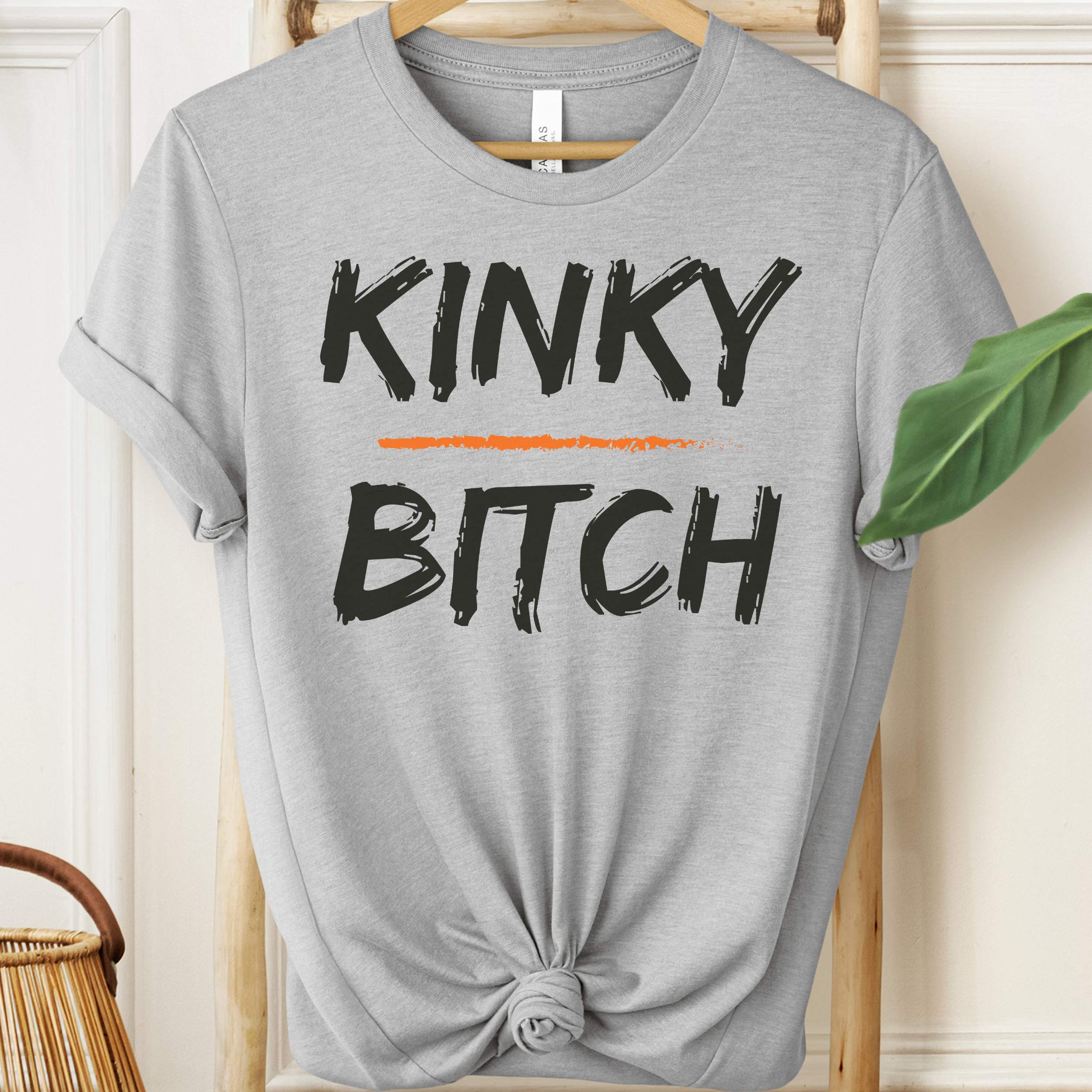 Gray t-shirt with 'KINKY BITCH' text on a hanger.