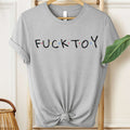 Gray t-shirt with 'FUCKTOY' text on a hanger against a neutral background