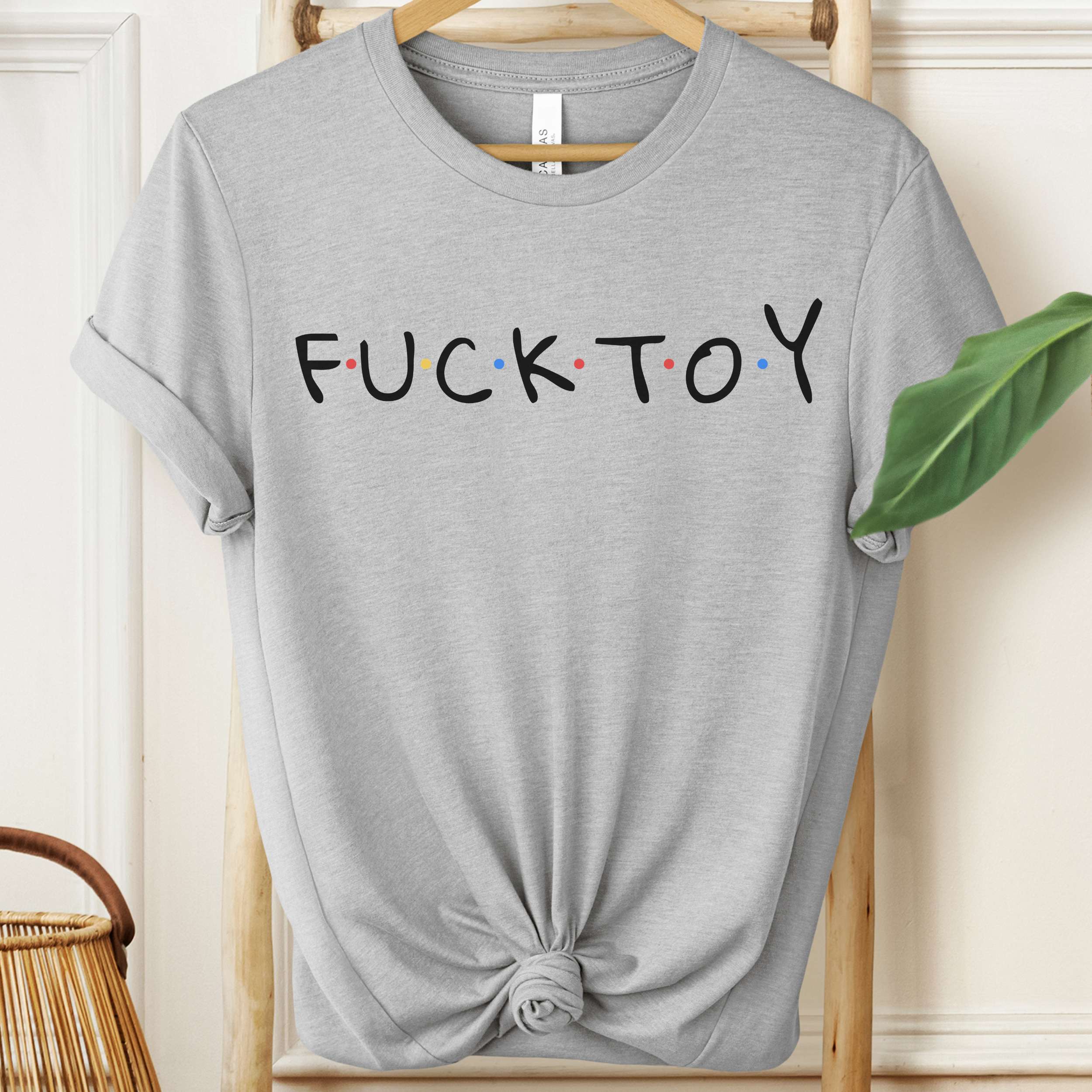 Gray t-shirt with 'FUCKTOY' text on a hanger against a neutral background