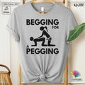 Gray t-shirt with graphic design and text 'Begging for a Pegging' on a hanger.