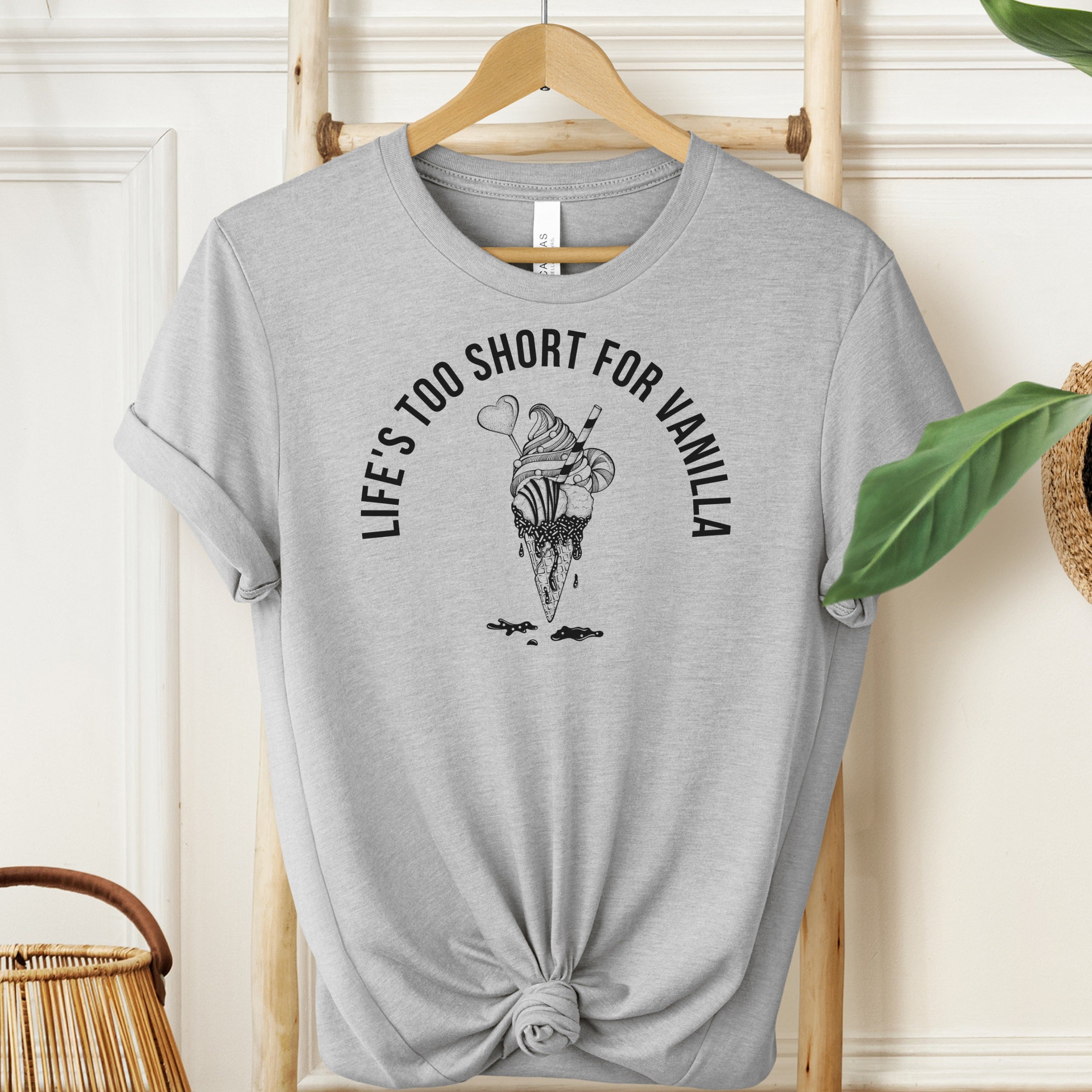 Gray t-shirt with ice cream graphic and text on a hanger against a white wall.