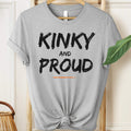 Gray t-shirt with 'Kinky and Proud' text on a hanger.