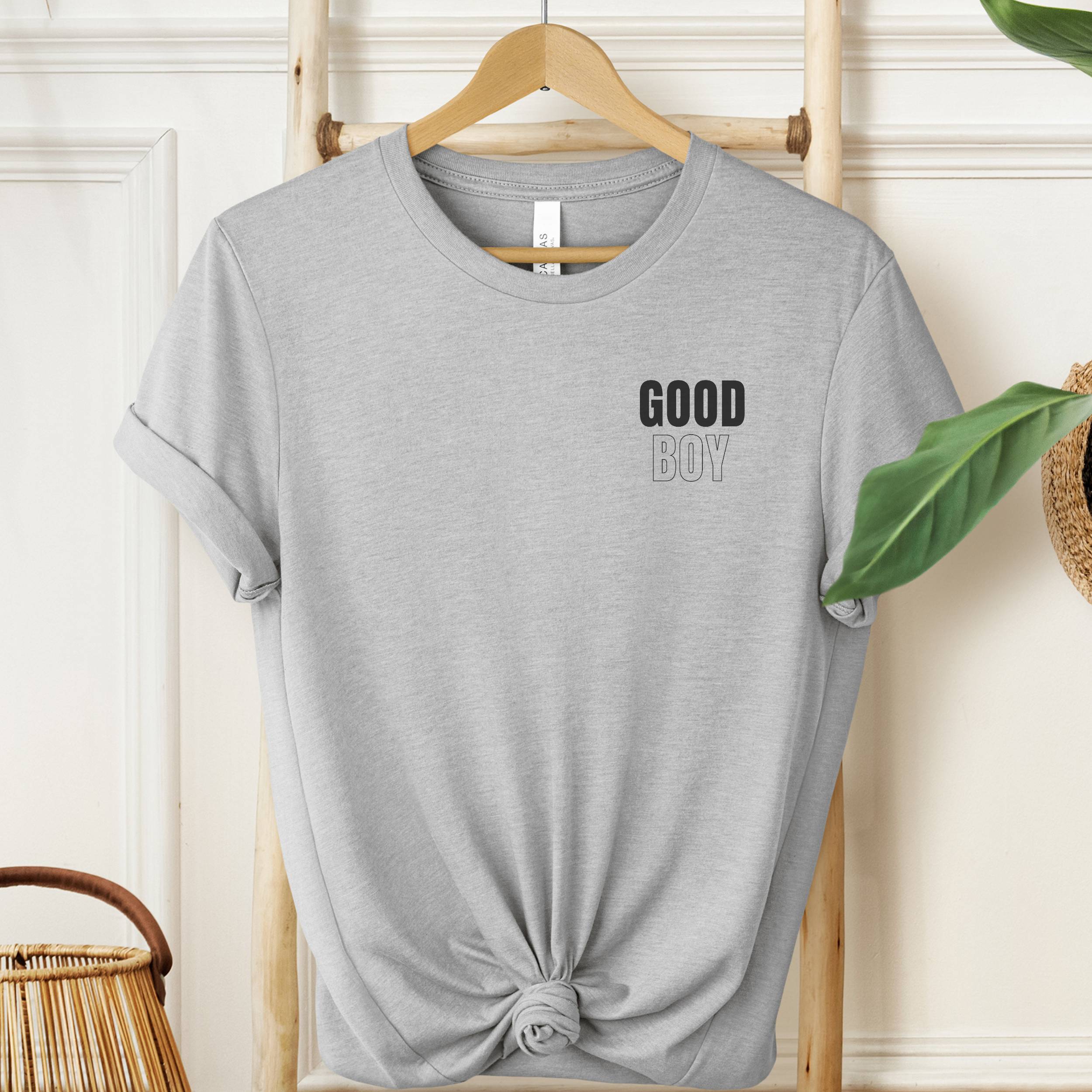 Gray t-shirt with 'GOOD BOY' text on a hanger against a neutral background