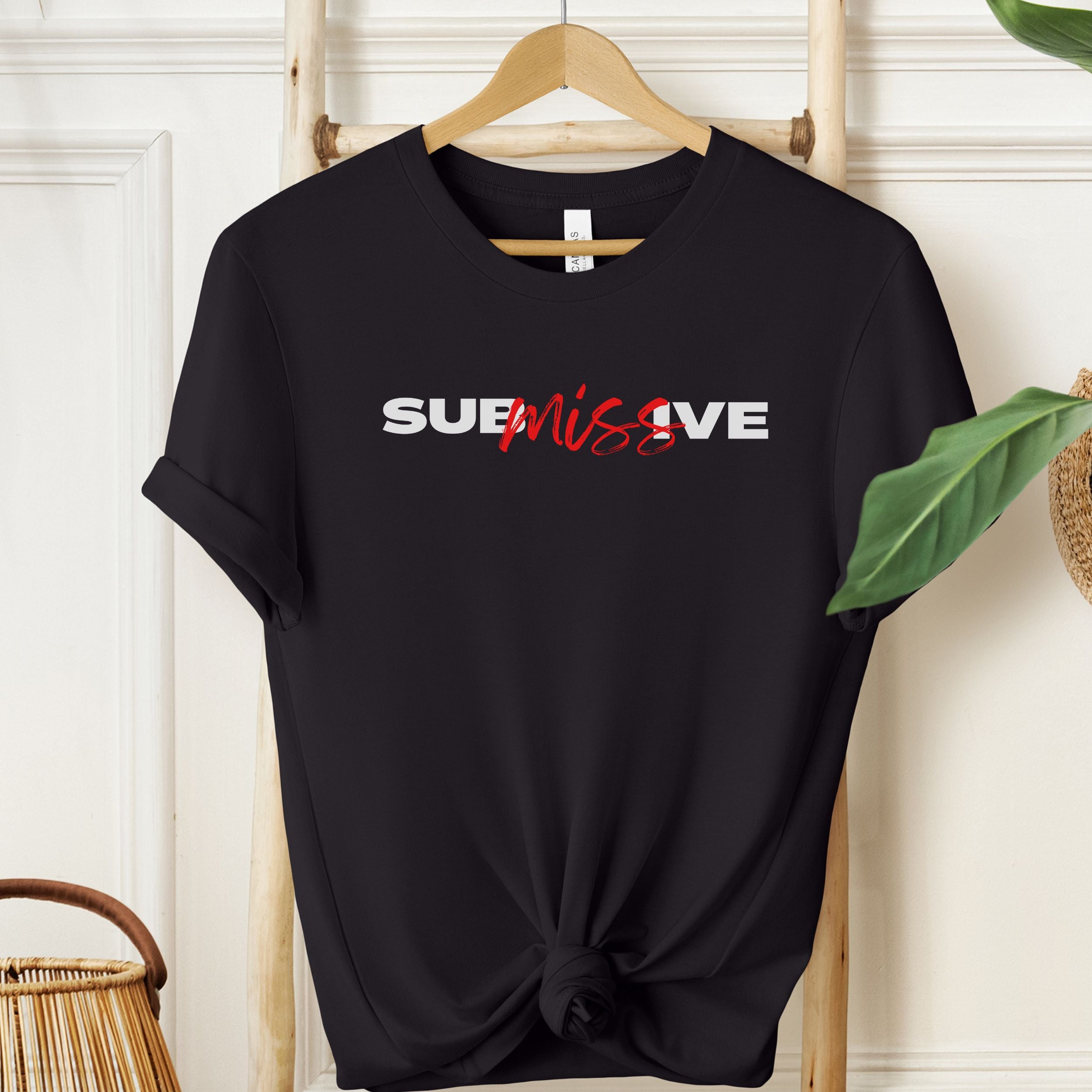 Black t-shirt with 'SUBMISSIVE' text on a hanger against a white wall.