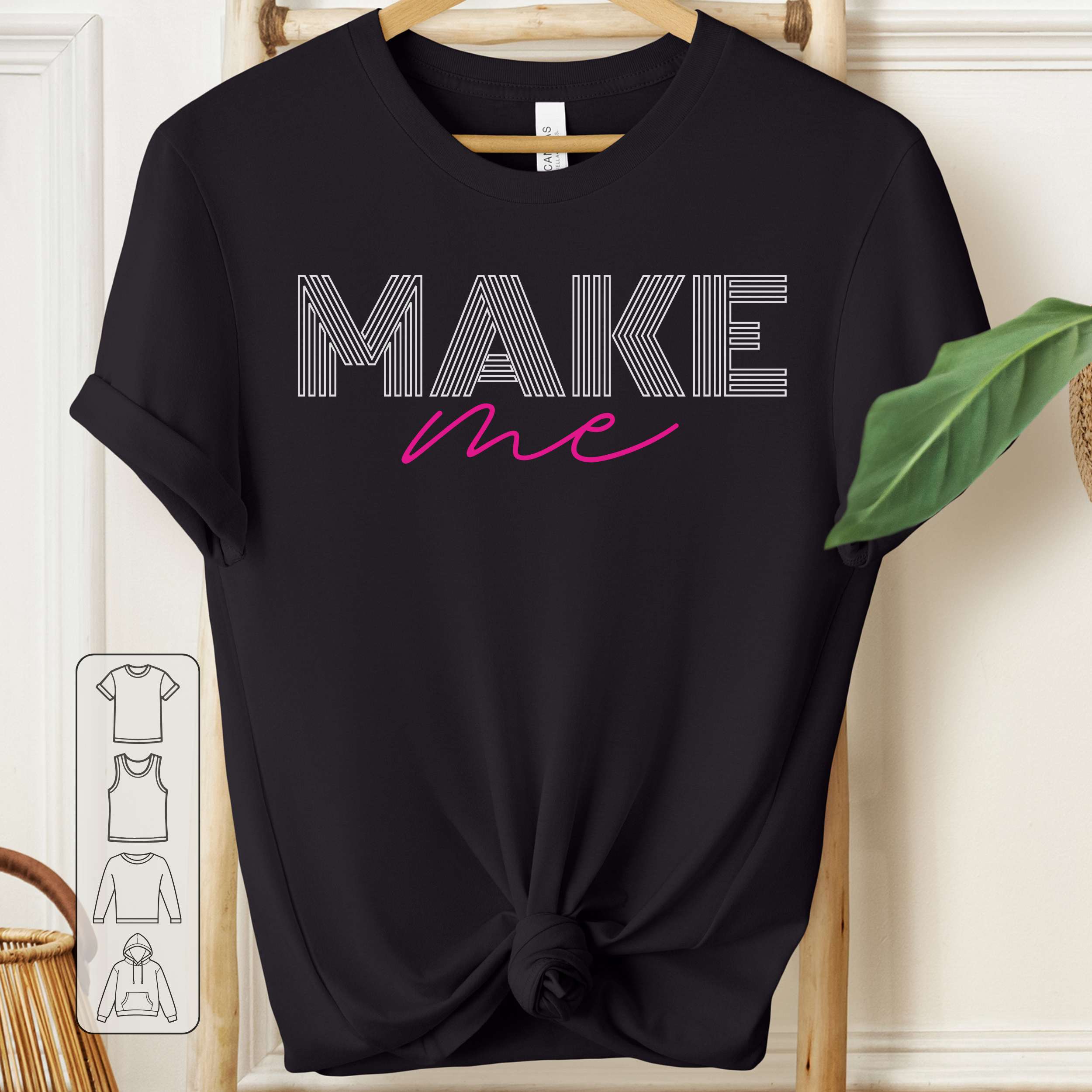 Black t-shirt with 'MAKE me' text on a hanger against a white wall.