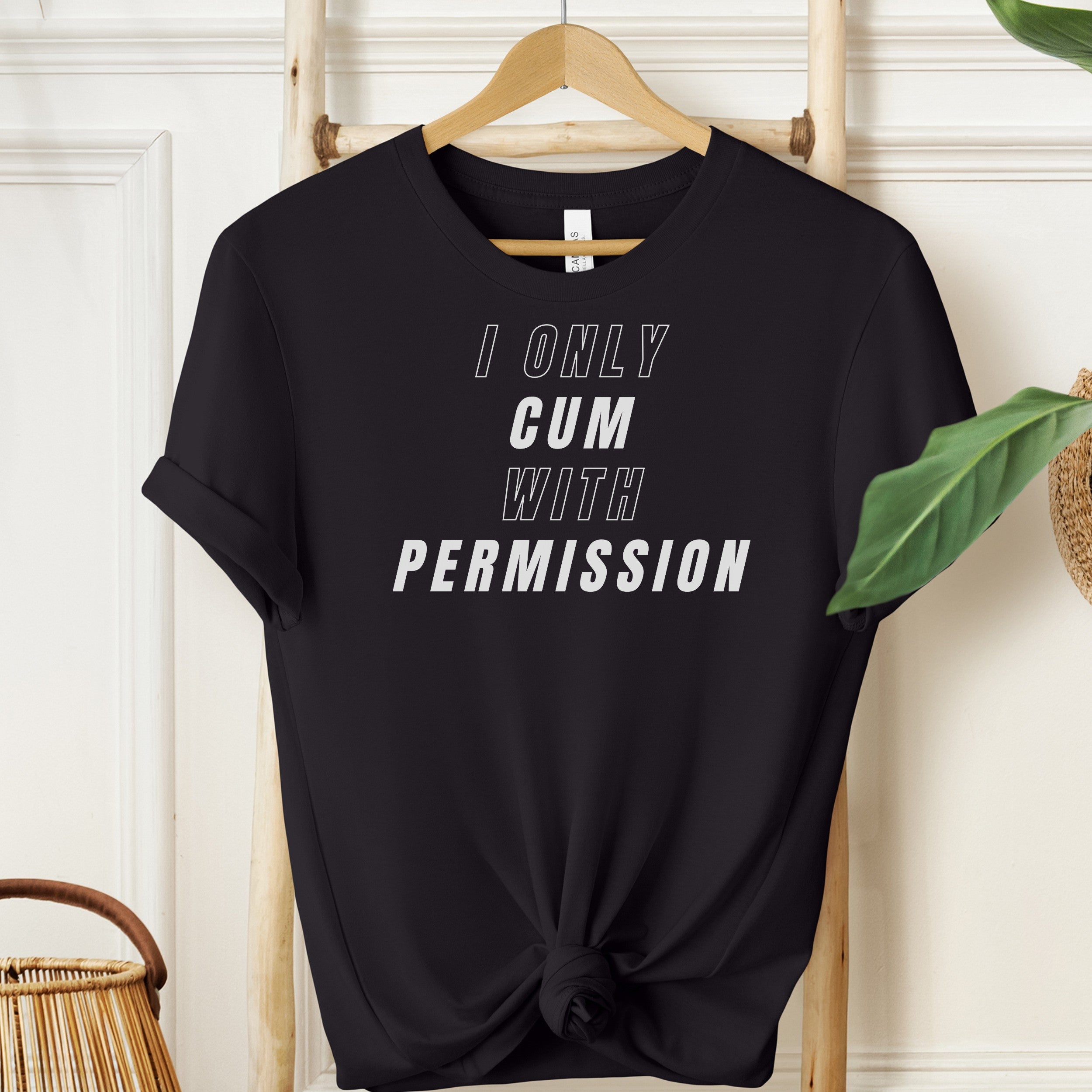 Black t-shirt with text 'I ONLY CUM WITH PERMISSION' on a hanger against a white wall.