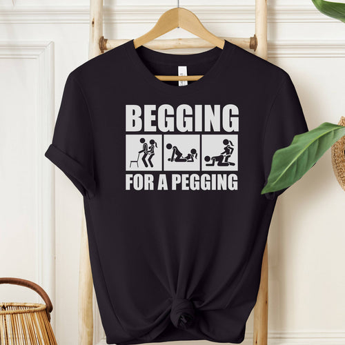 Black t-shirt with white text and graphics on a hanger against a white wall.