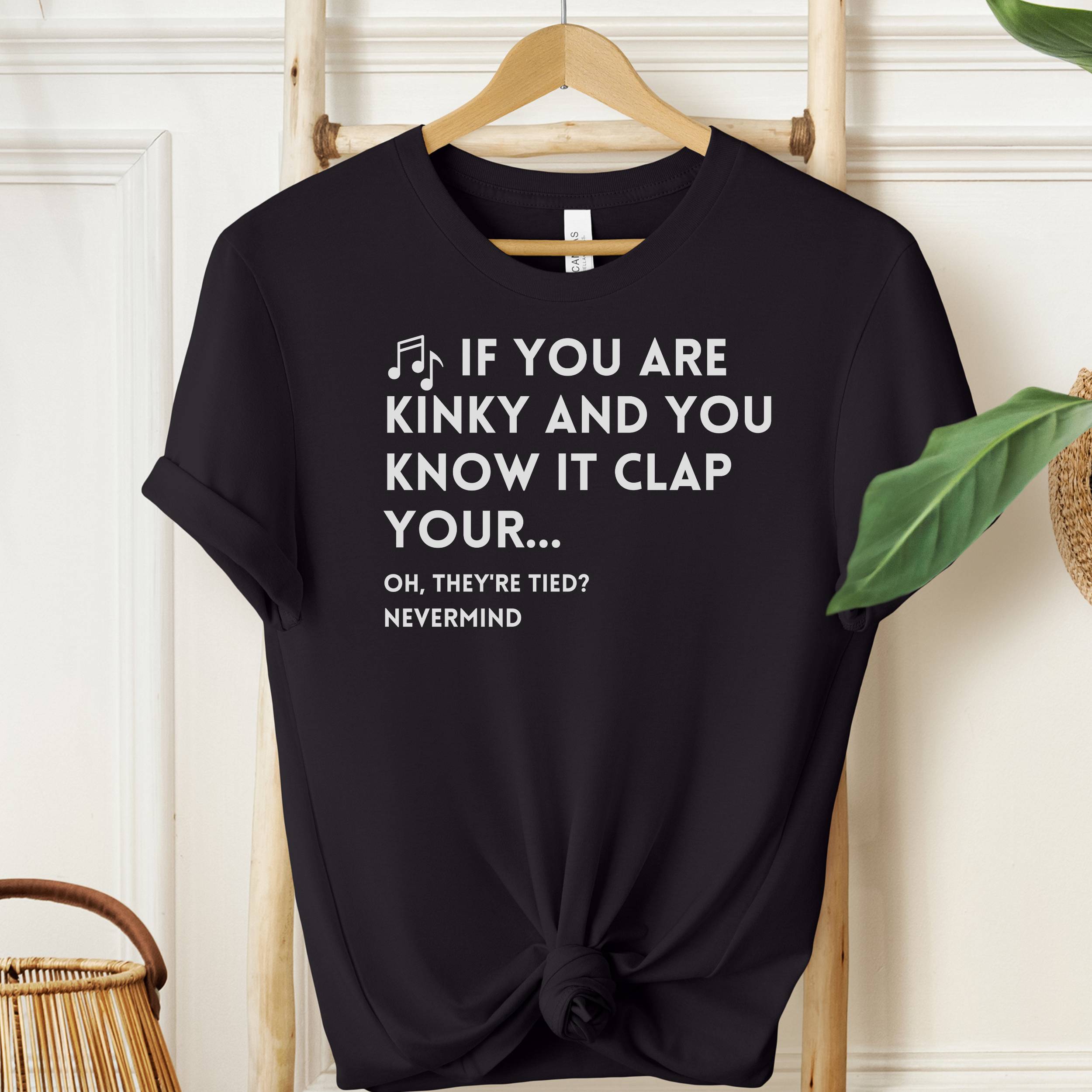 Black t-shirt with humorous text design on a wooden hanger against a white wall.