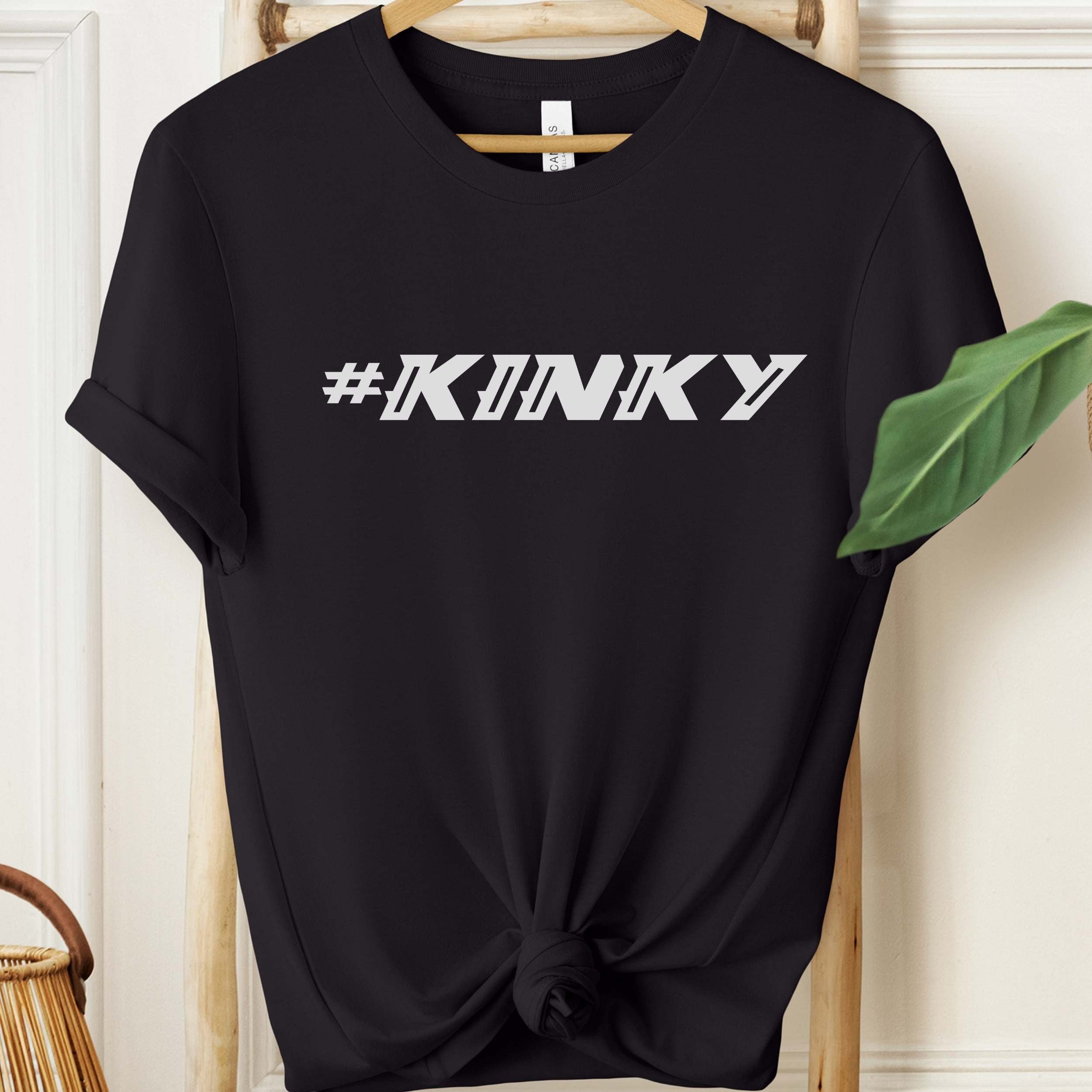 Black t-shirt with '#KINKY' text on a hanger against a neutral background