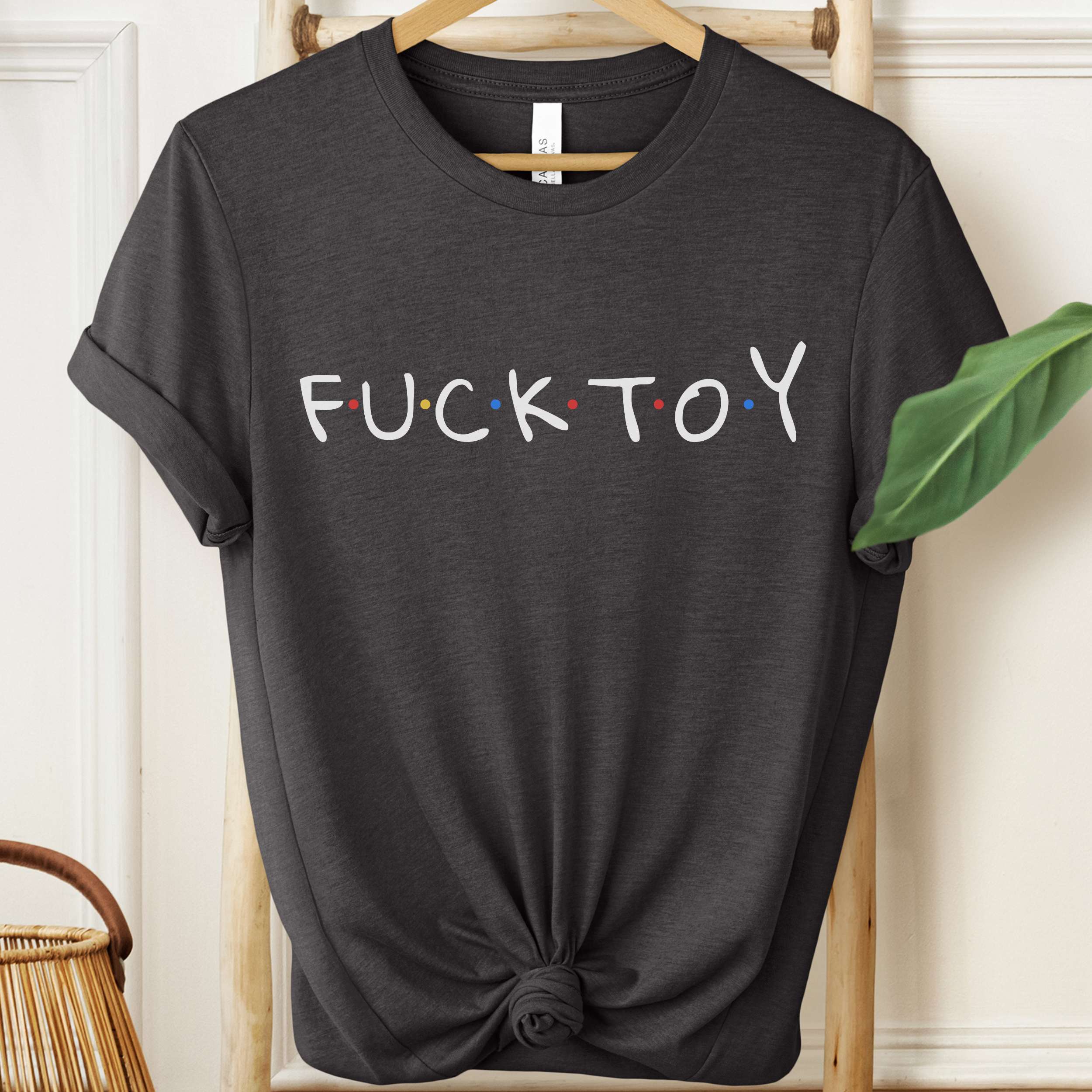 Black t-shirt with 'FUCK TOY' text on a hanger against a white wall.