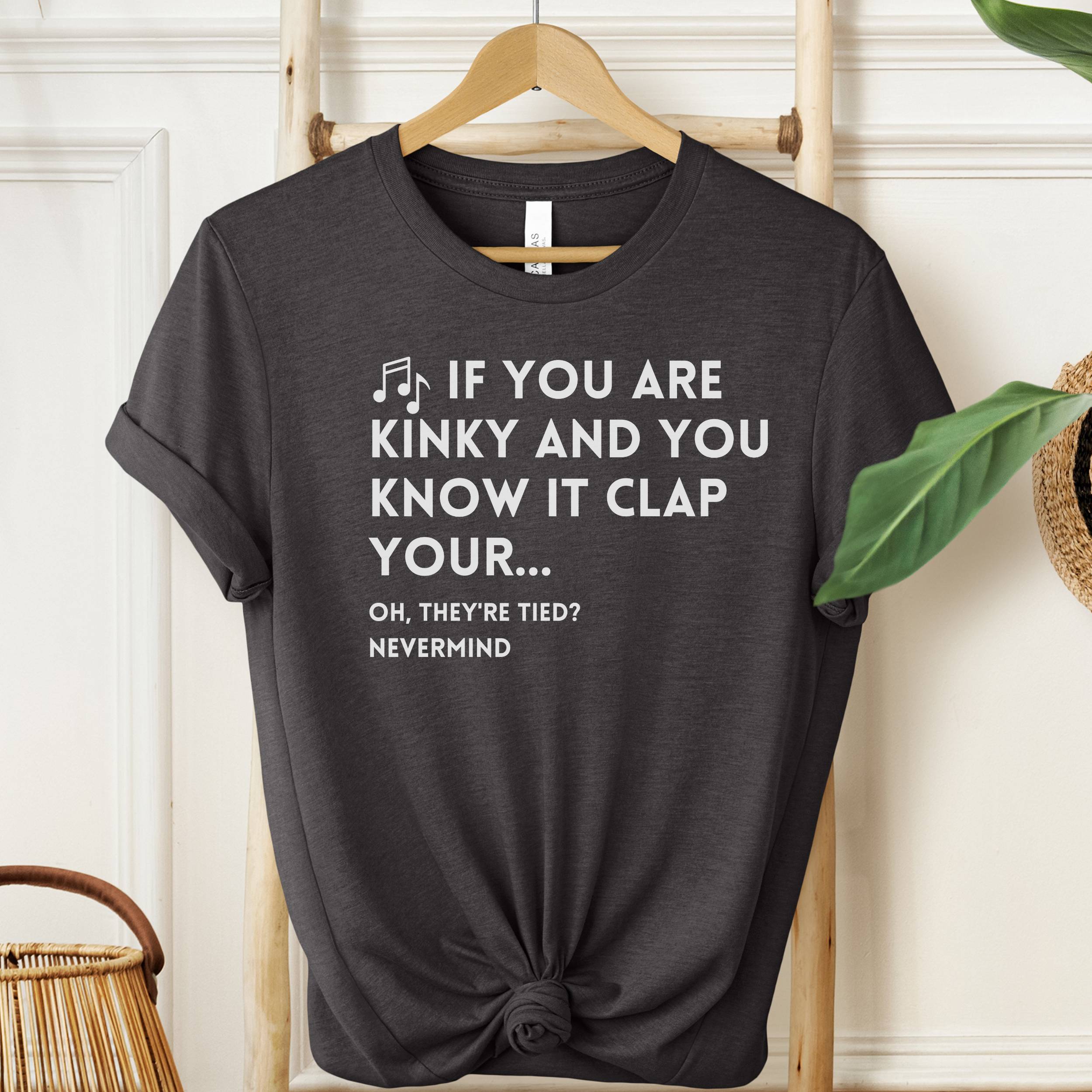 Black t-shirt with humorous text on a hanger against a neutral background