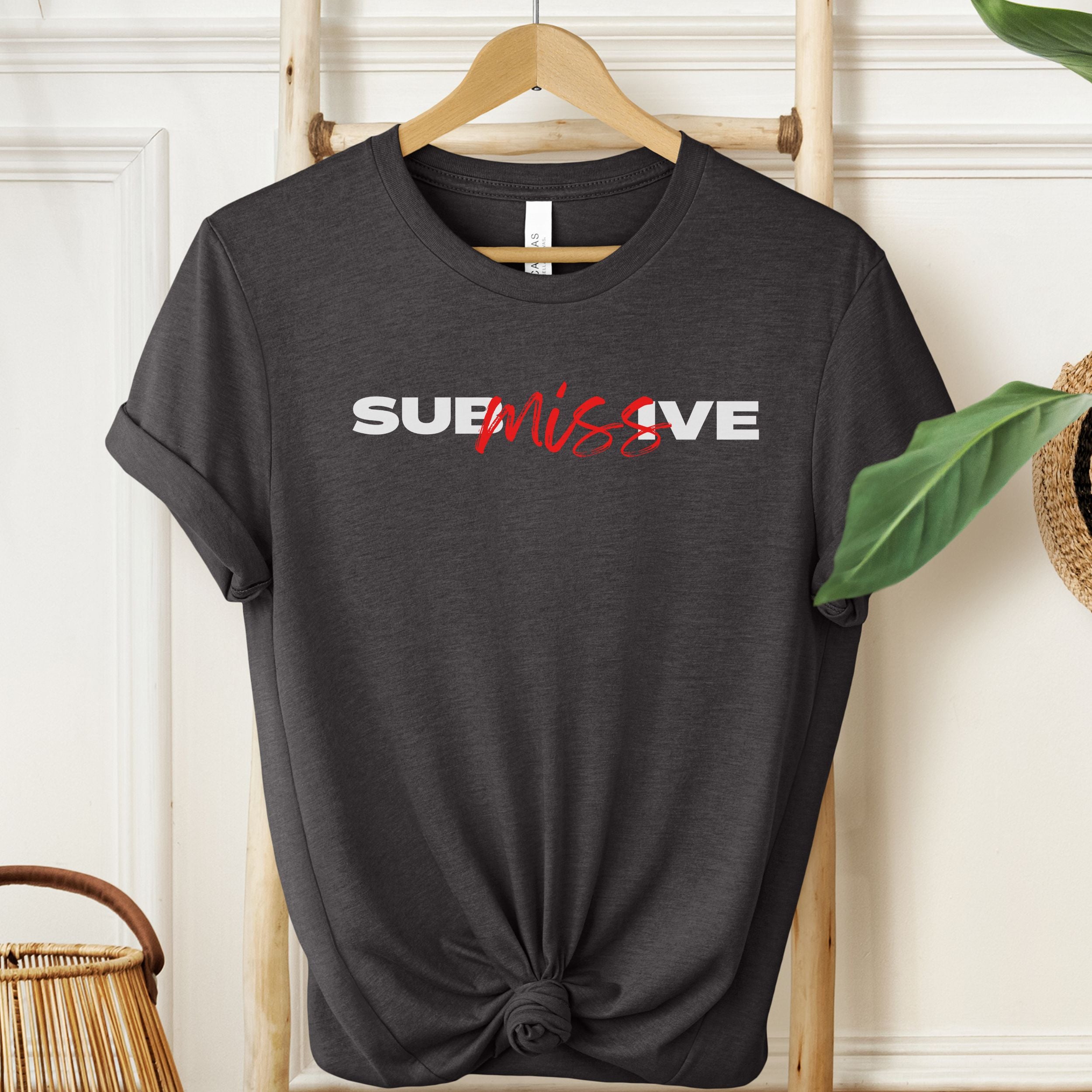 Dark Grey Heather t-shirt with 'SUBMISSIVE' text on a hanger against a white wall.