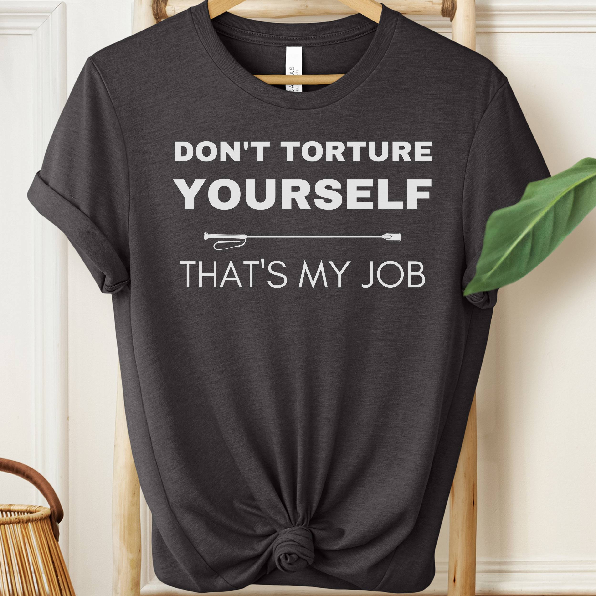 Black t-shirt with white text 'DON'T TORTURE YOURSELF THAT'S MY JOB' on a hanger.