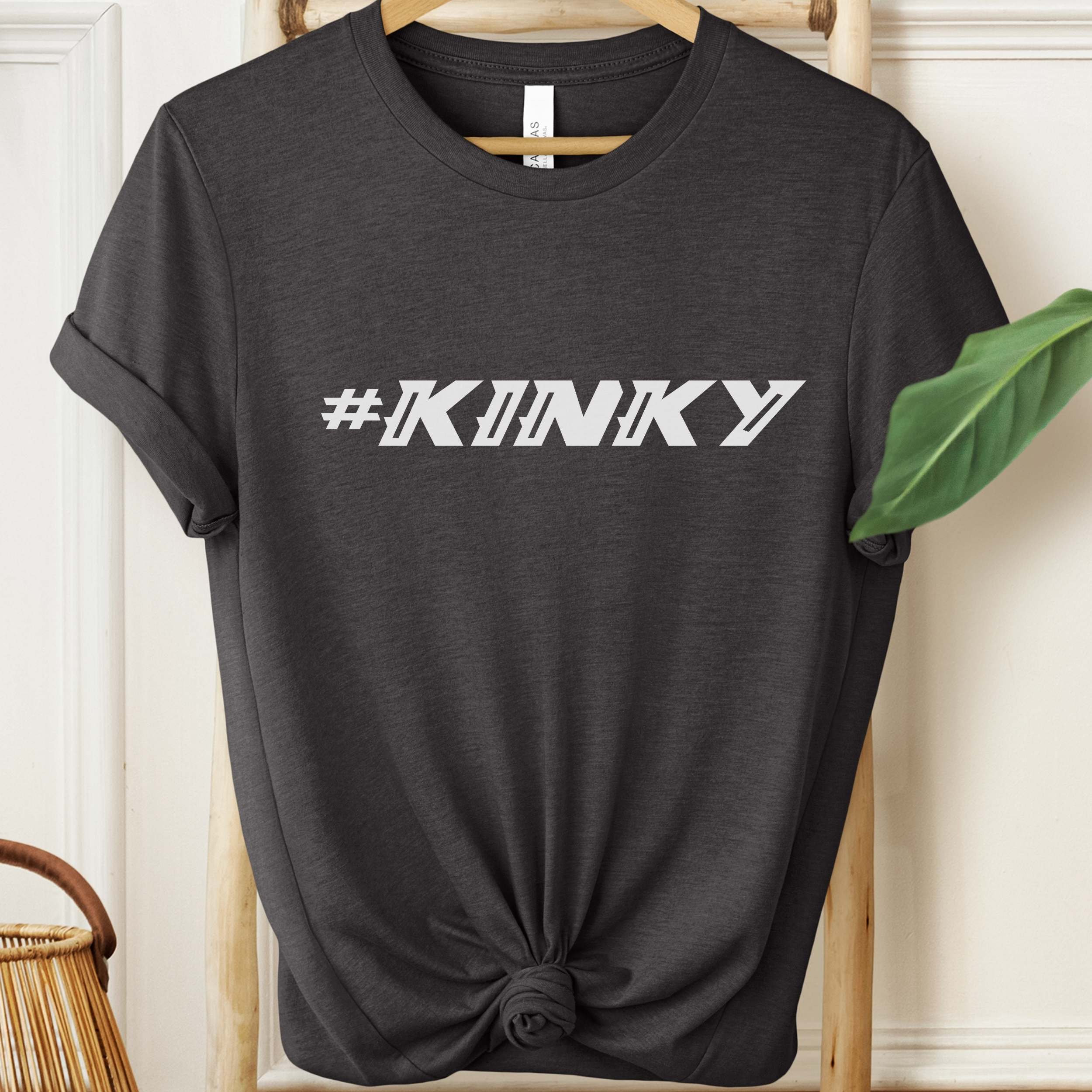 Black t-shirt with '#KINKY' text on a hanger against a neutral background
