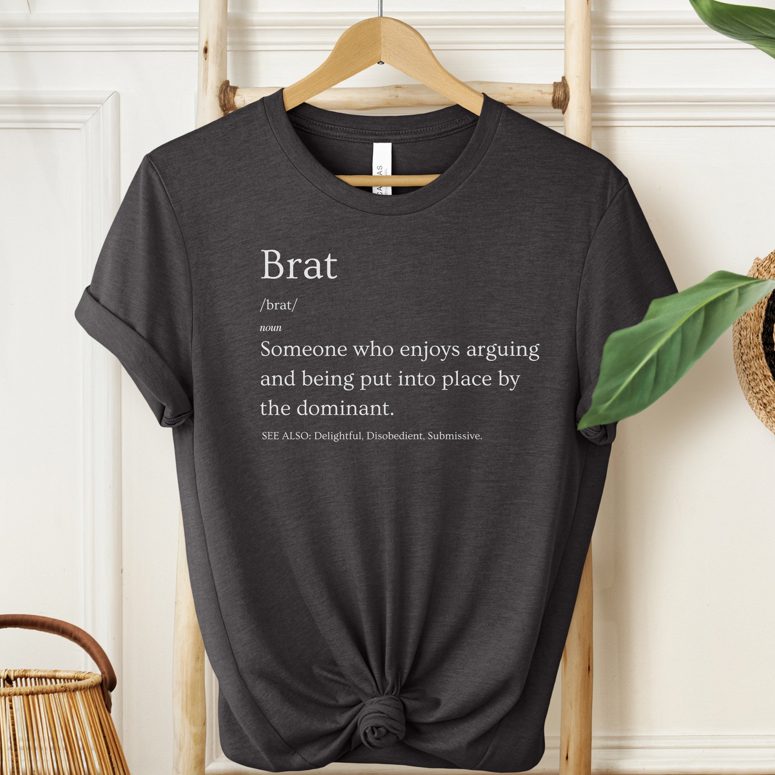 Black t-shirt with text on a hanger against a white wall.