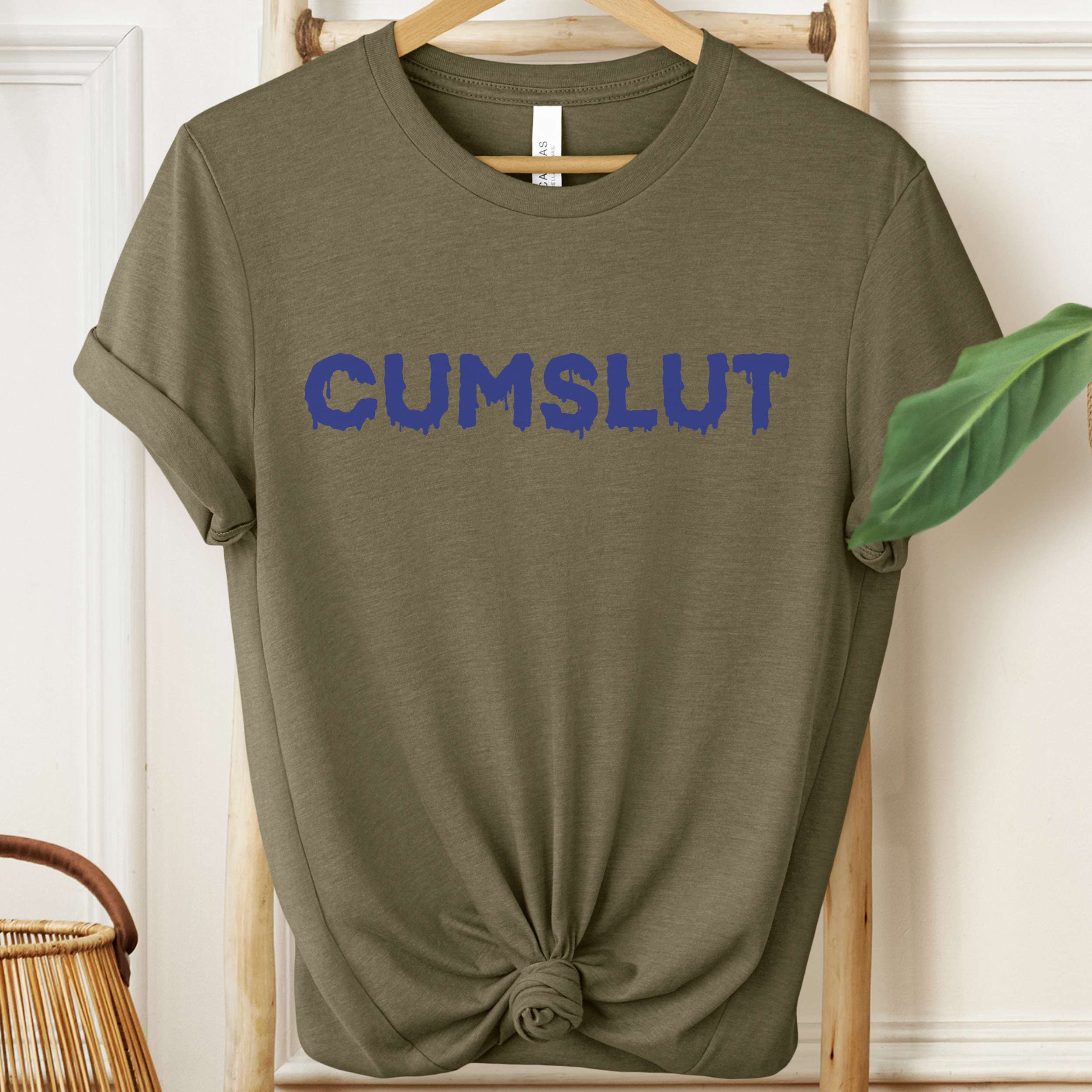 Green t-shirt with 'CUMSLUT' printed in blue on a hanger.