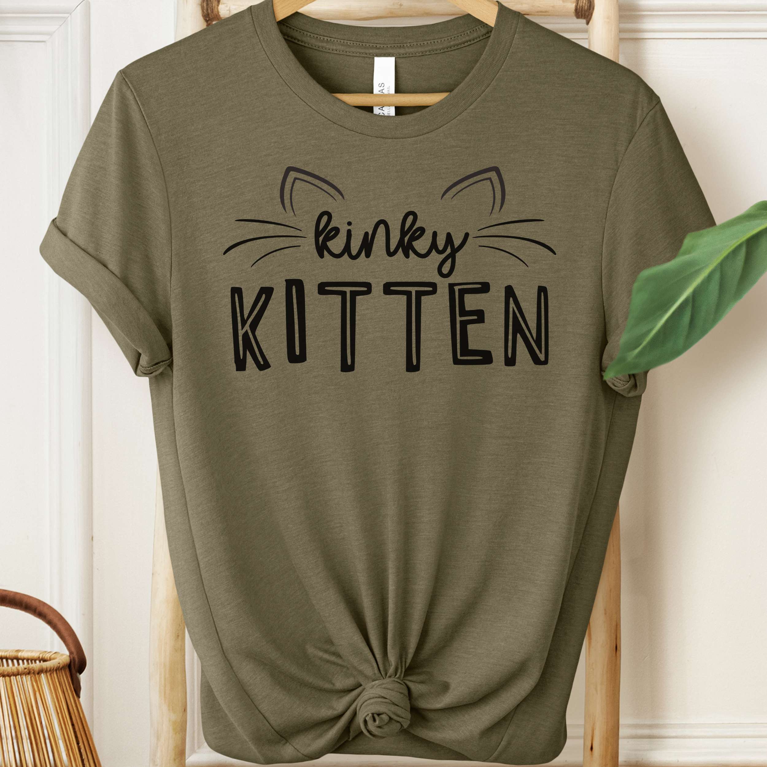 Olive green t-shirt with 'kinky KITTEN' text on a hanger.