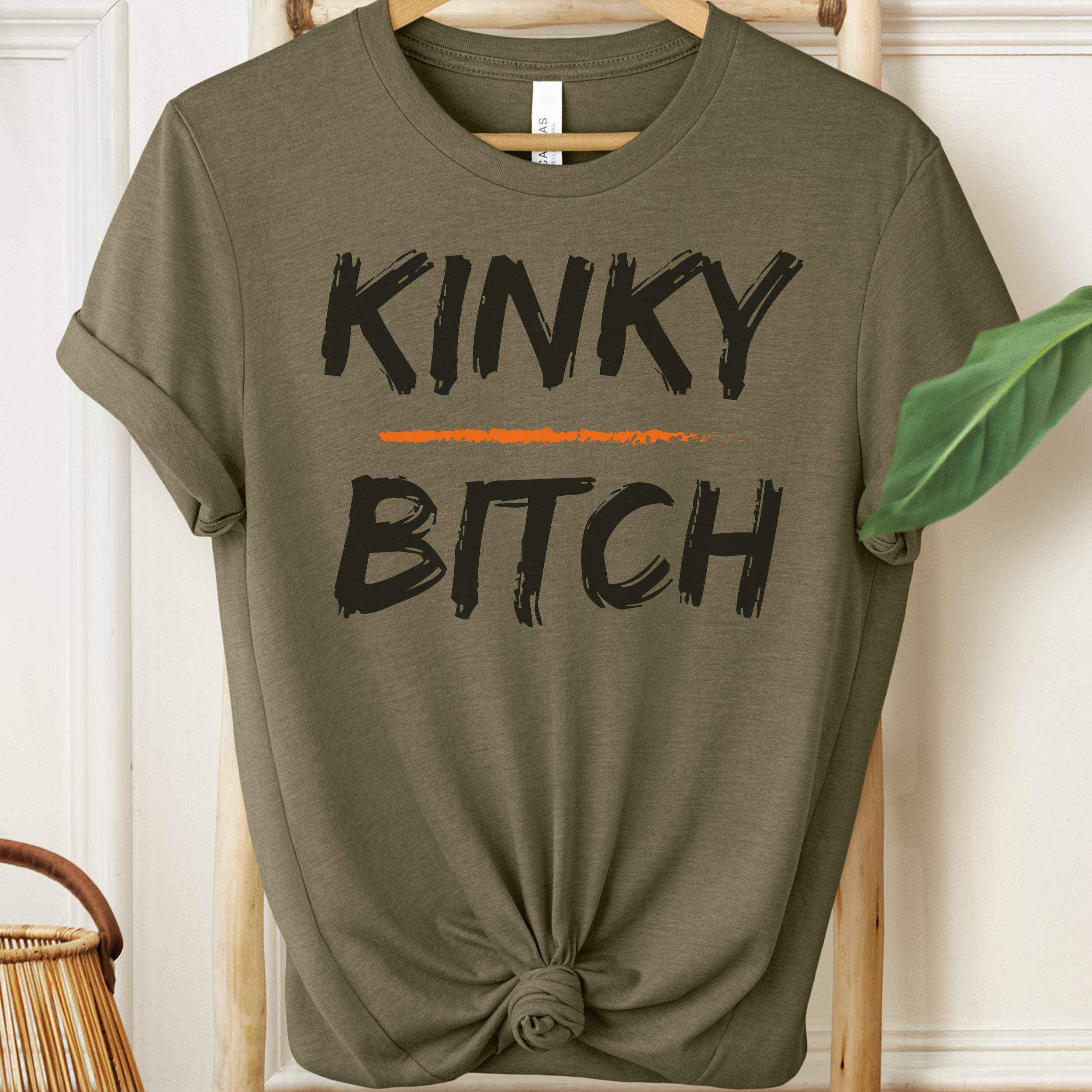 Olive green t-shirt with 'KINKY BITCH' text on a hanger.