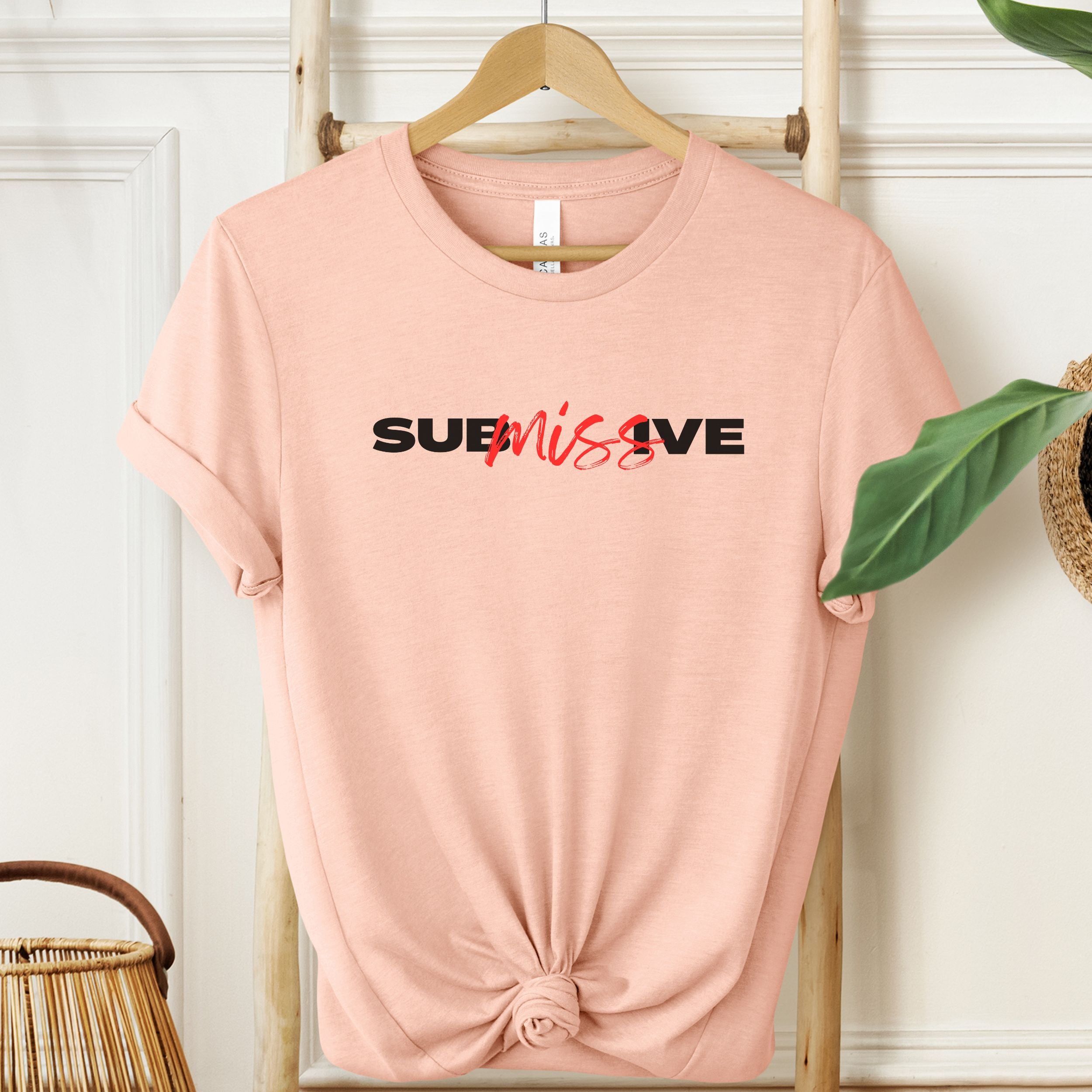 Light cream unisex shirt featuring the word “SUBMISSIVE” in bold black letters, with “miss” handwritten in red script.