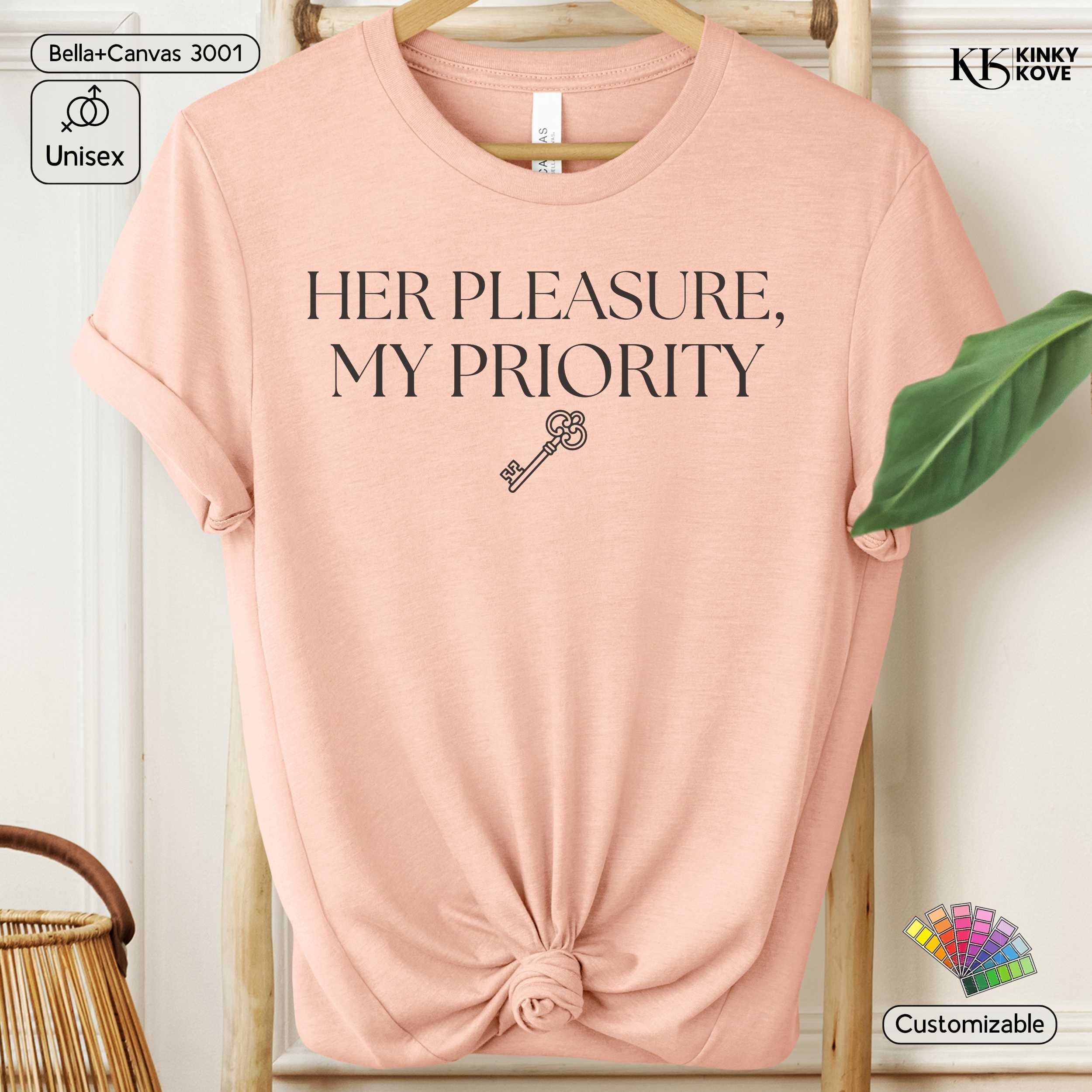 Pink t-shirt with 'HER PLEASURE, MY PRIORITY' text and key graphic on a hanger.