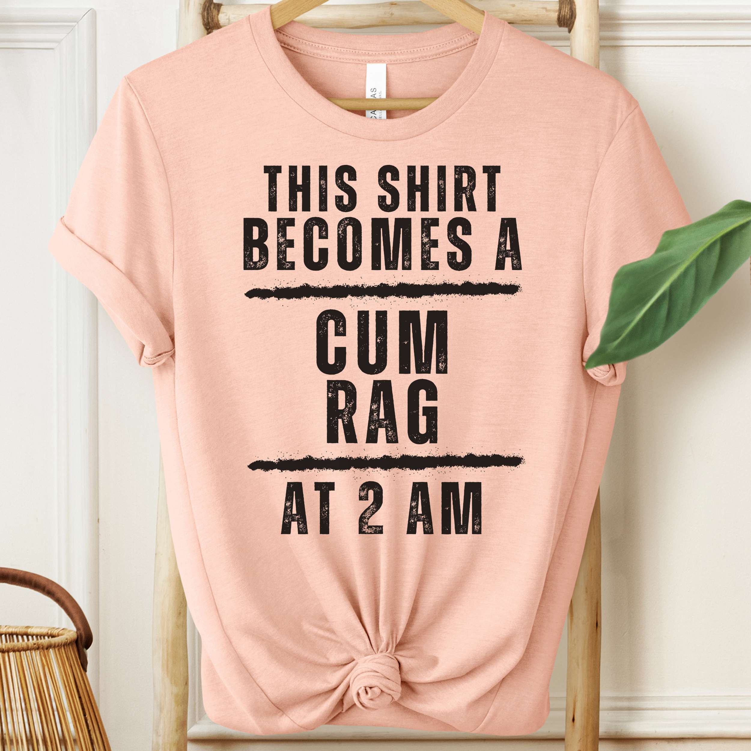Pink t-shirt with black text on a hanger against a white wall.