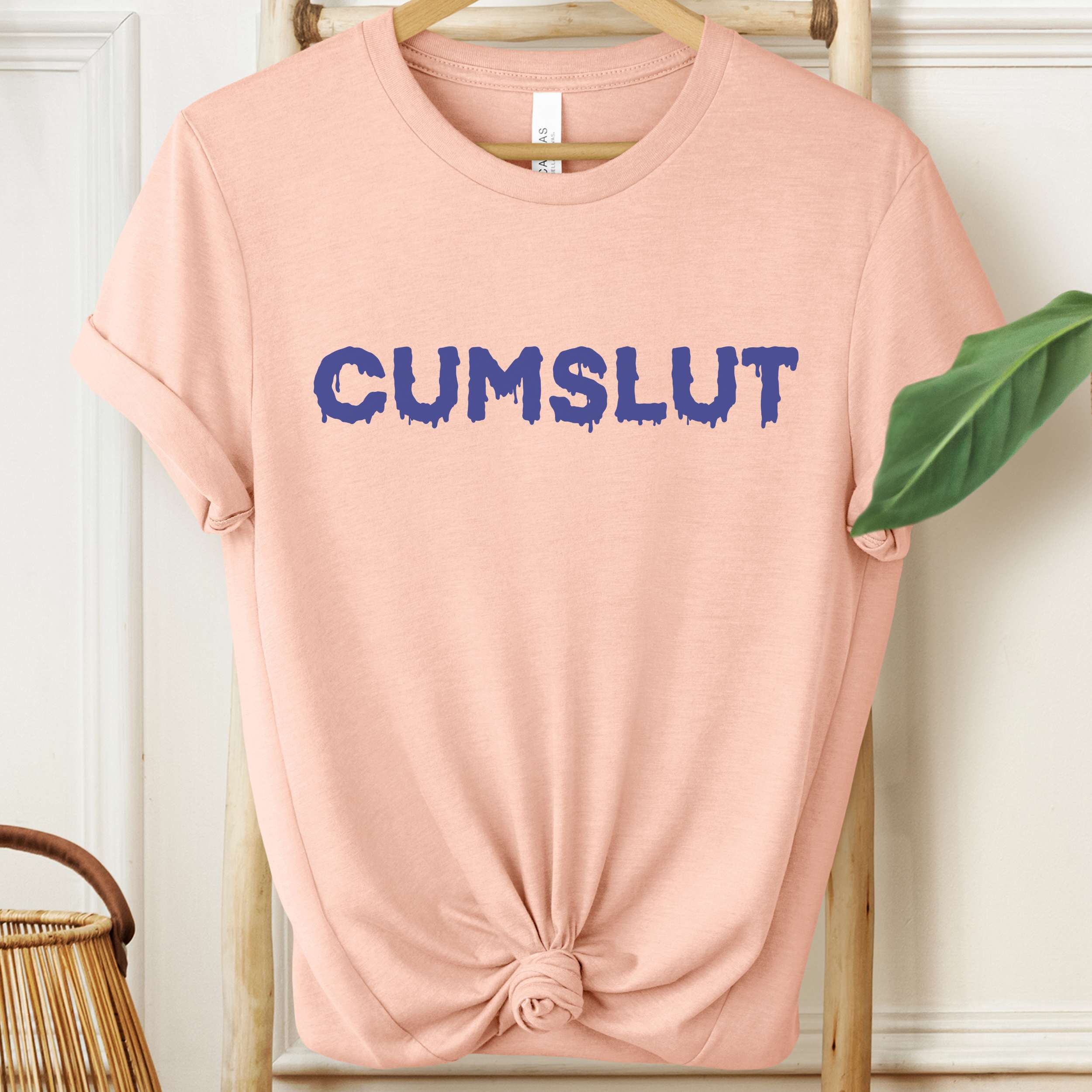 Pink t-shirt with 'CUMSLUT' printed in blue on a hanger.