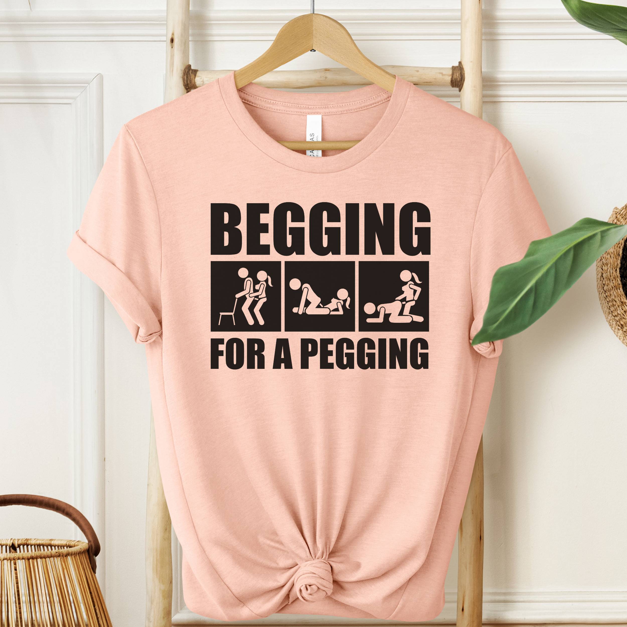 Heather Peach Begging For A Pegging T-Shirt with black graphic print, bold unisex novelty shirt.