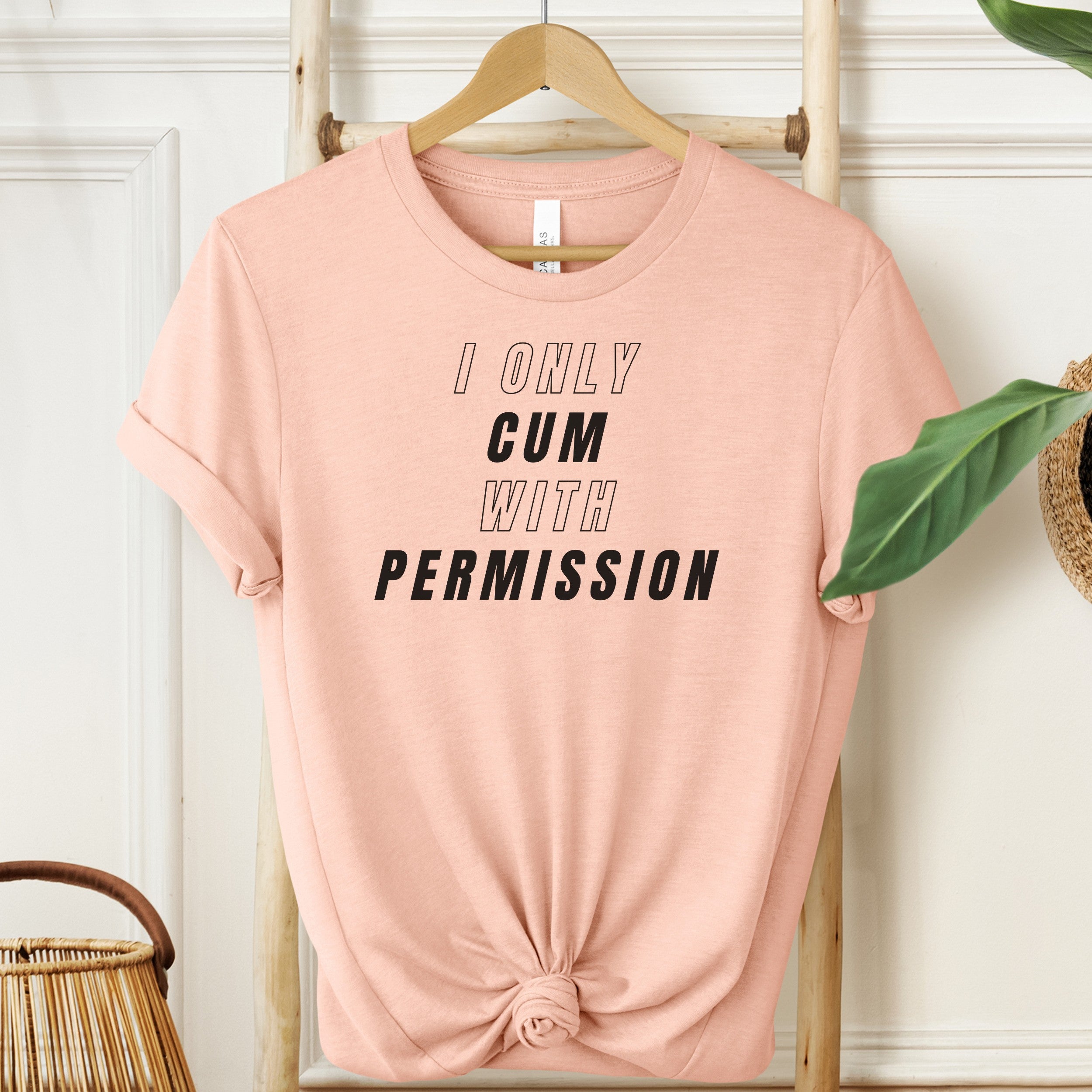 Pink t-shirt with text 'I ONLY GUM WITH PERMISSION' on a hanger against a white wall.