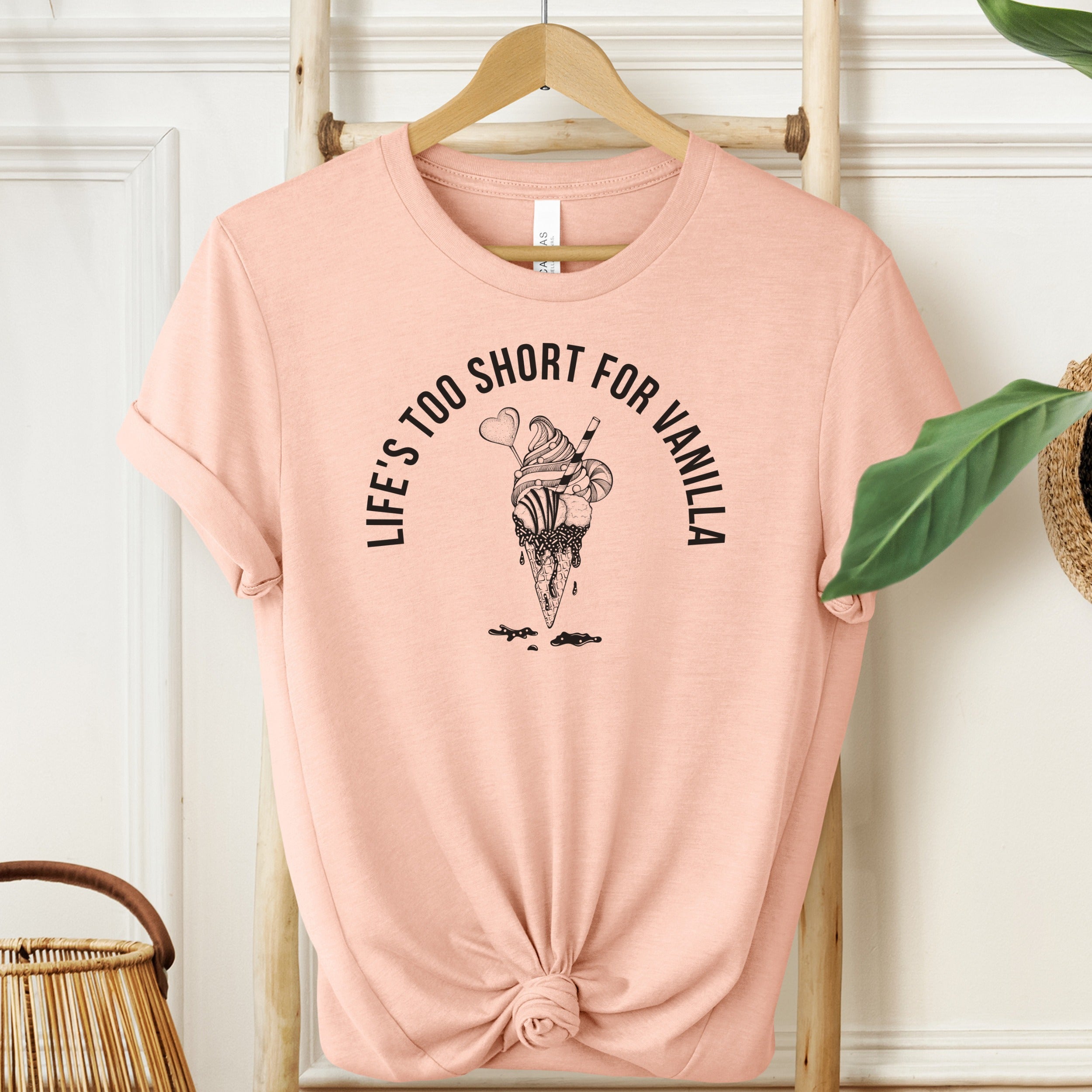 Pink t-shirt with ice cream graphic and text on a hanger against a white wall.