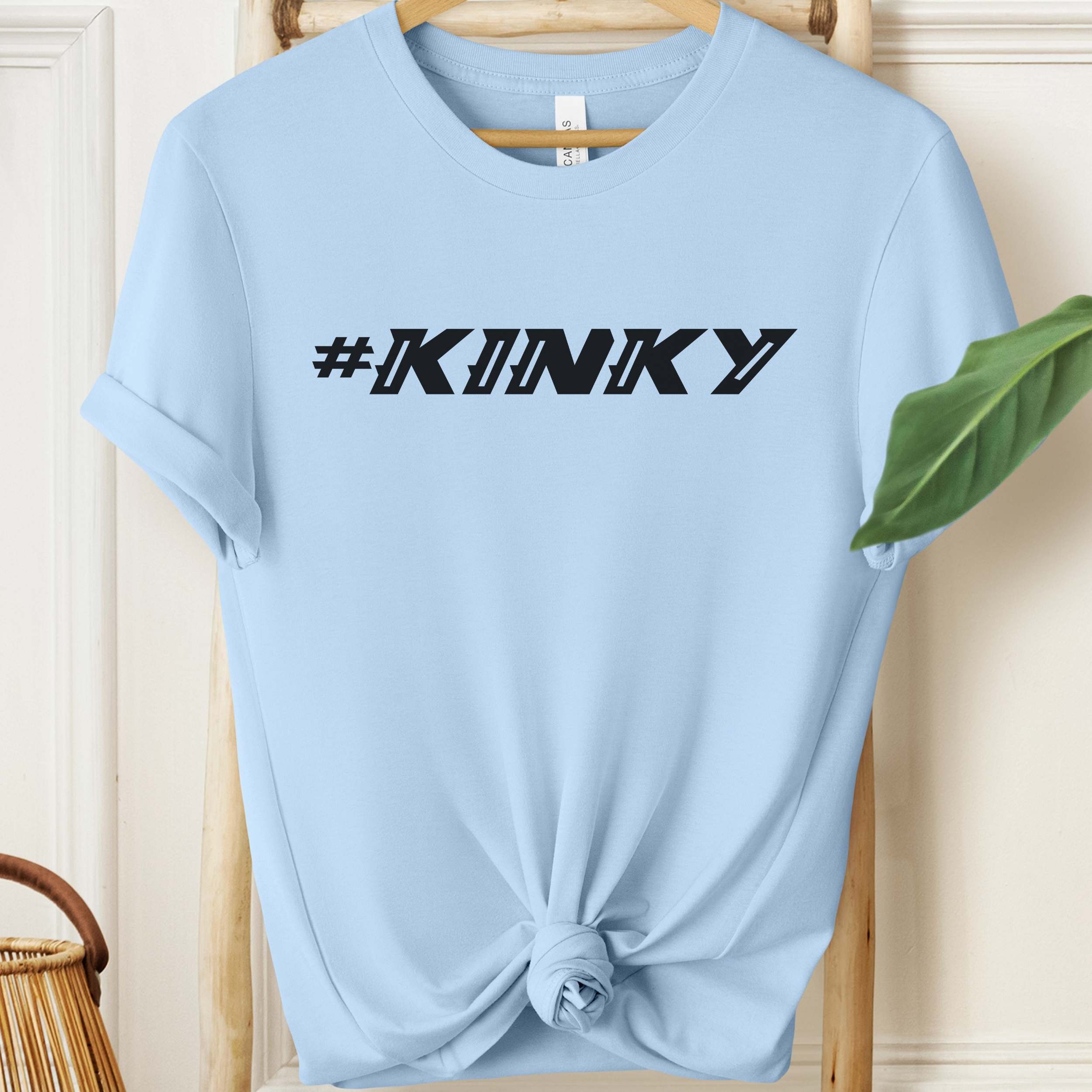 Light blue t-shirt with '#KINKY' text on a wooden hanger.