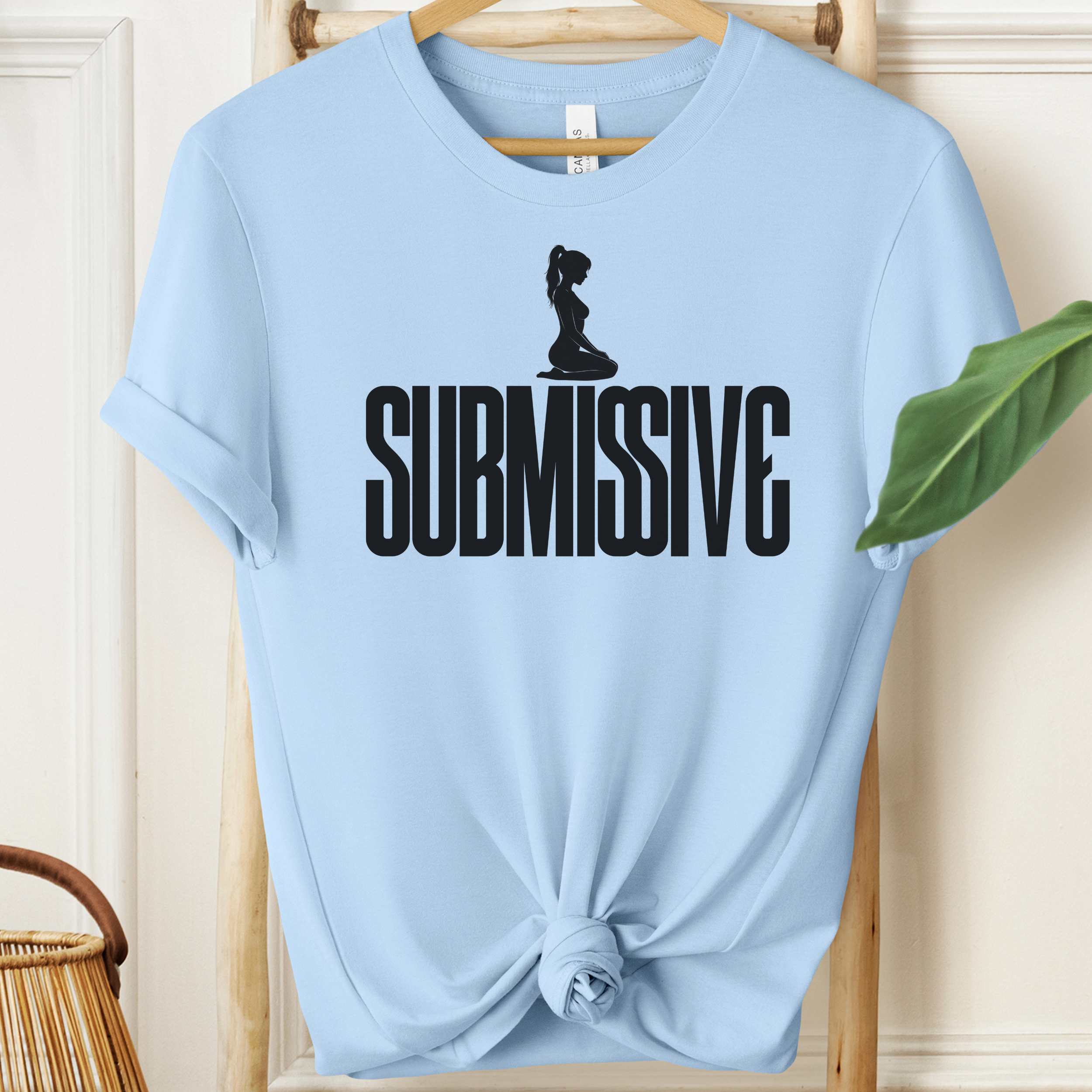 Light blue t-shirt with 'SUBMISSIVE' text and graphic on a wooden hanger.