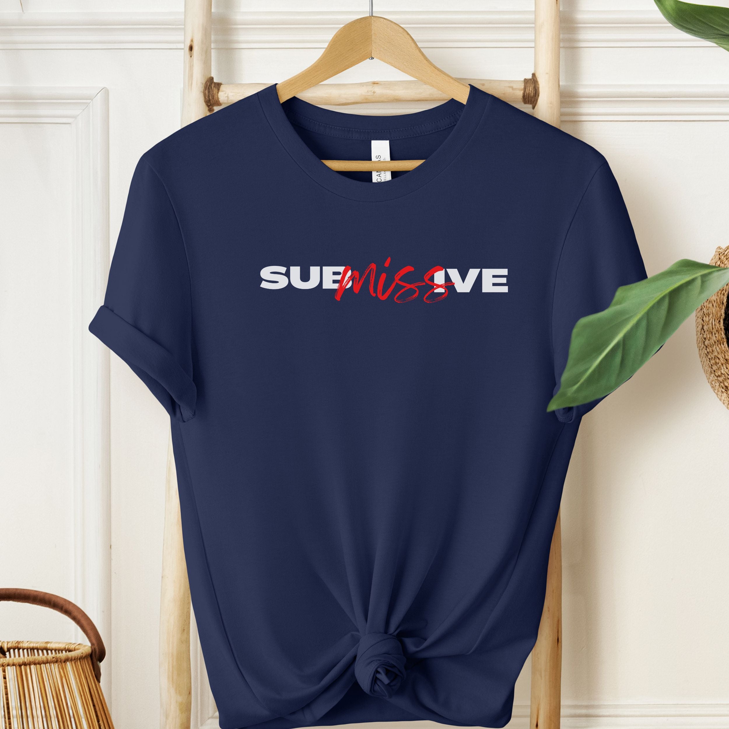 Navy blue t-shirt with 'SUBMISSIVE' text on a hanger against a white wall.