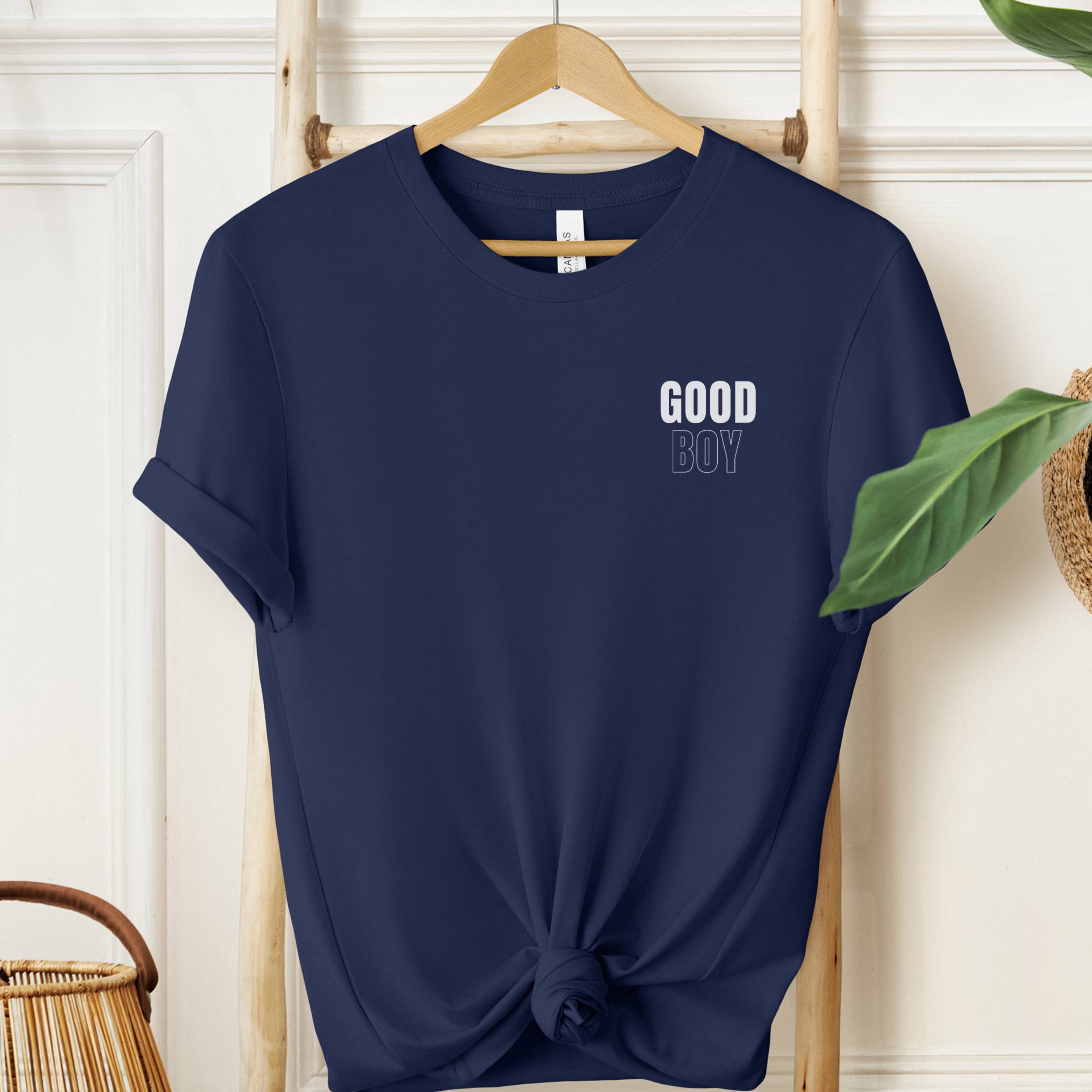 Navy blue t-shirt with 'GOOD BOY' text on a hanger against a white wall.
