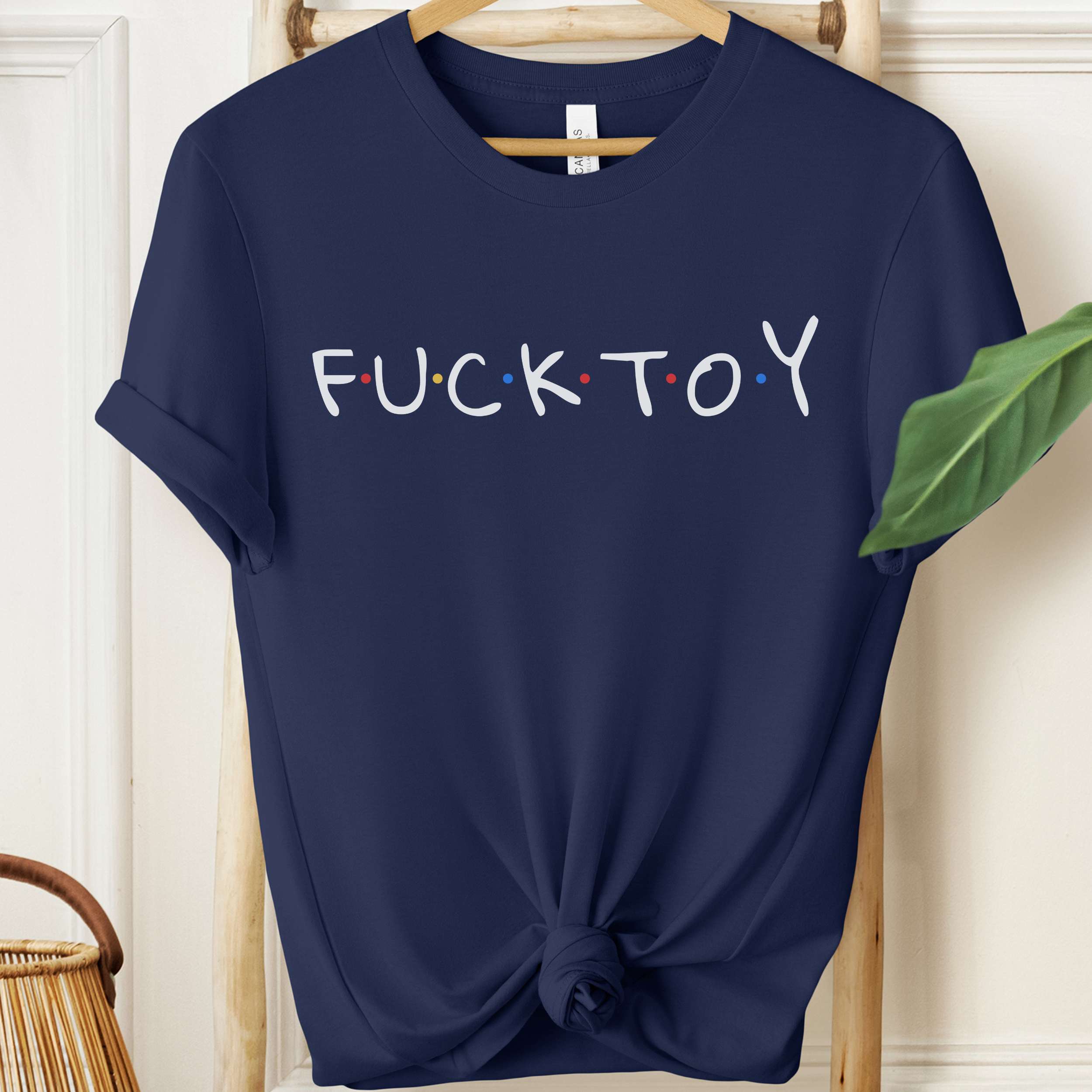 Navy blue t-shirt with 'FUCKTOY' text on a hanger against a white wall.