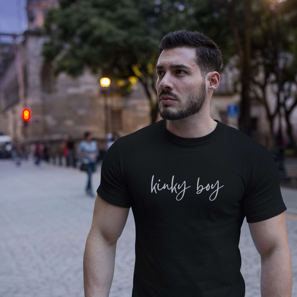 Man wearing a black t-shirt with 'kinky boy' text on a city street.