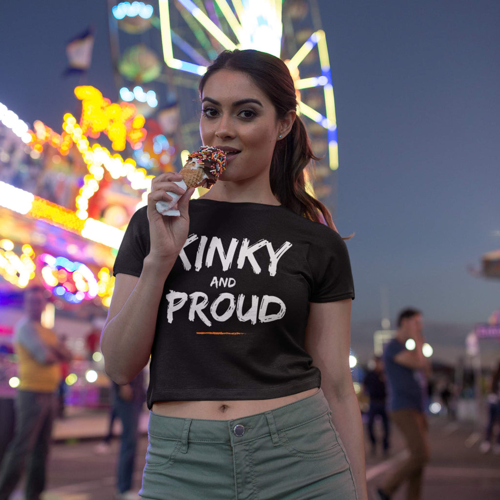 Woman wearing a 'Kinky and Proud' shirt at a carnival with a Ferris wheel in the background.