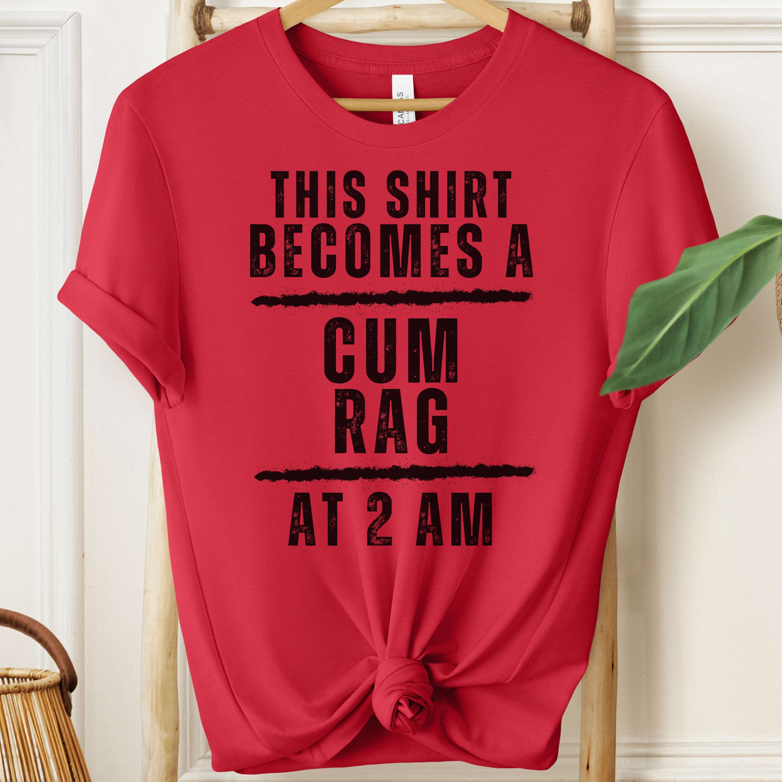 Red t-shirt with black text on a hanger against a white wall.
