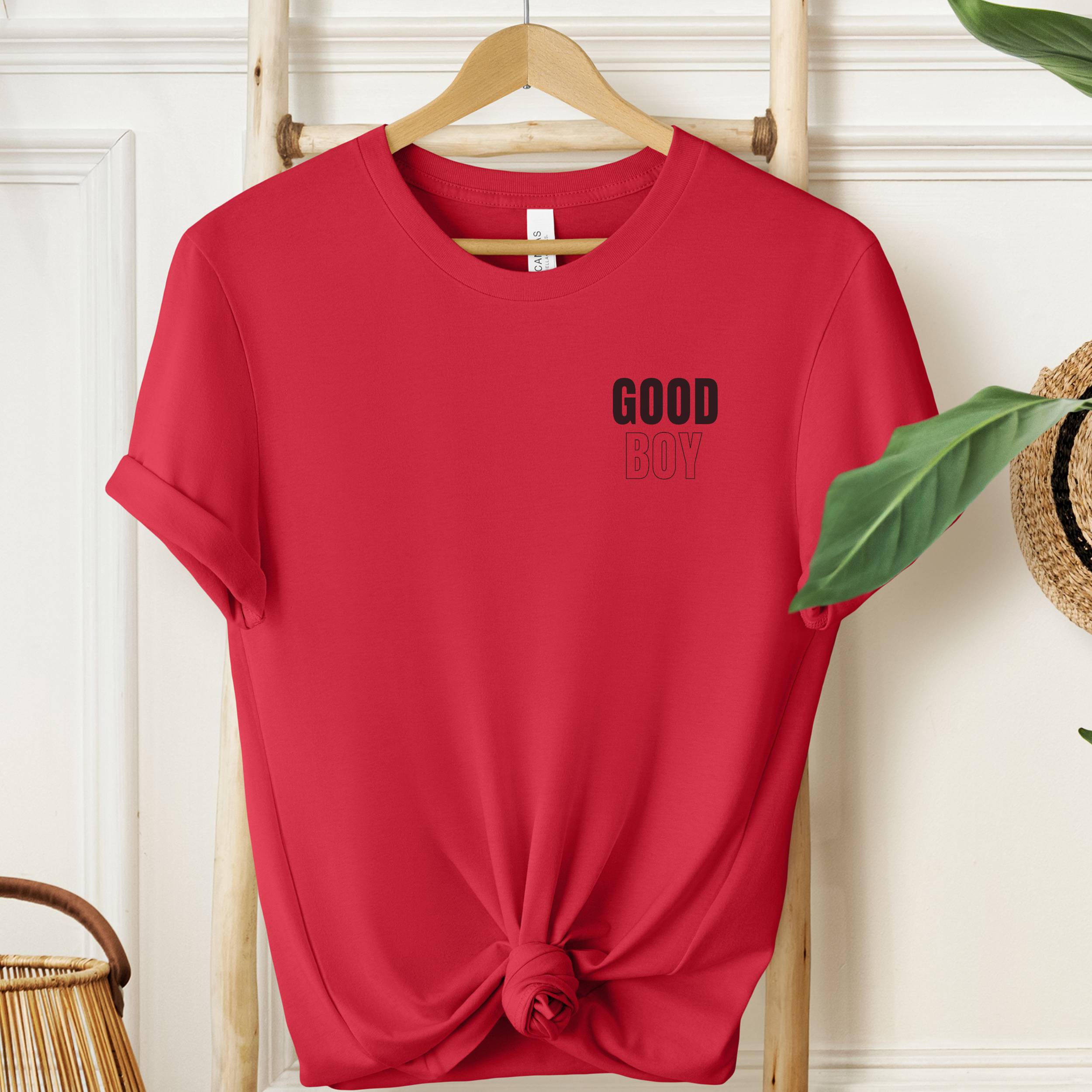 Red t-shirt with 'GOOD BOY' text on a wooden hanger against a white wall.