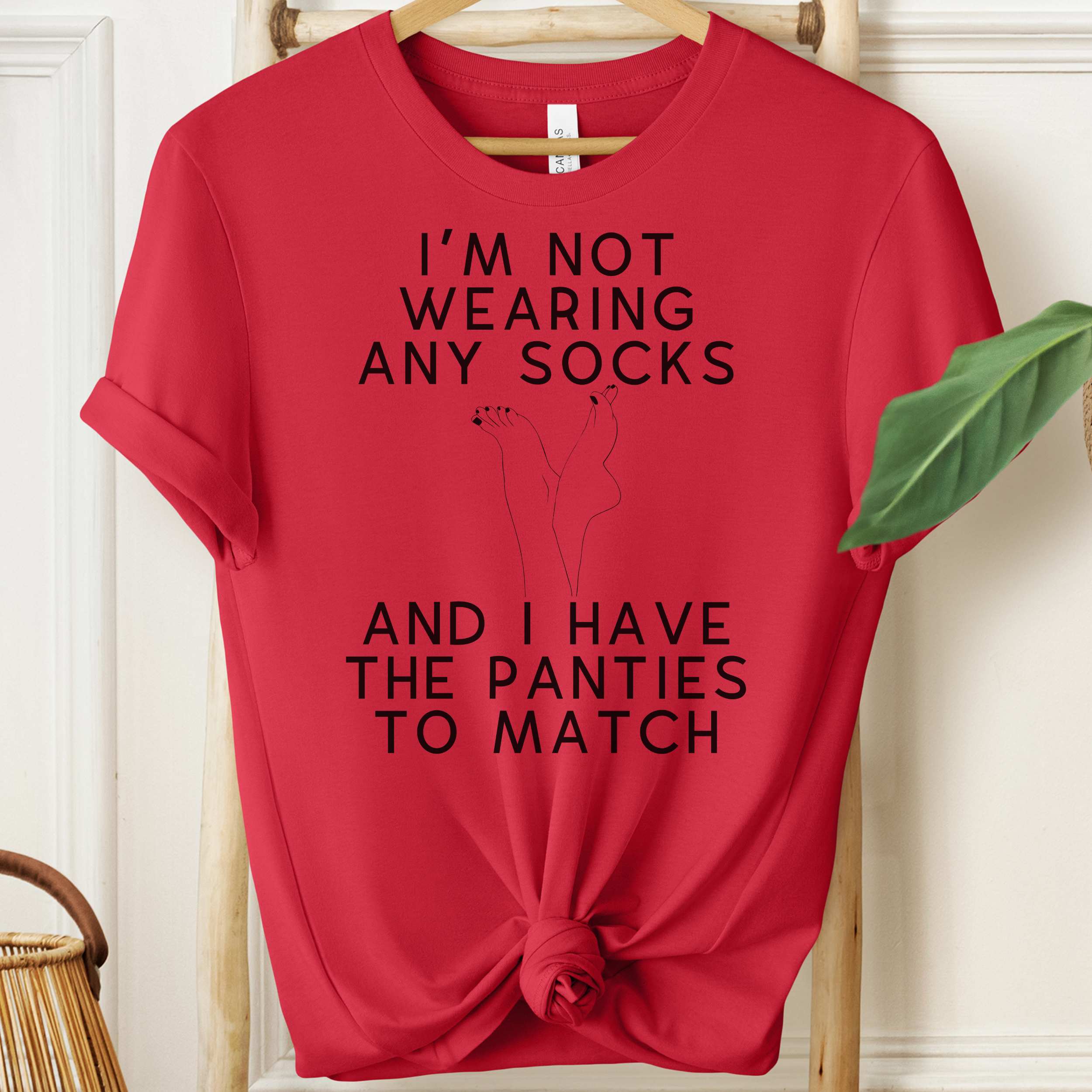Red t-shirt with humorous text design on a hanger against a white wall.