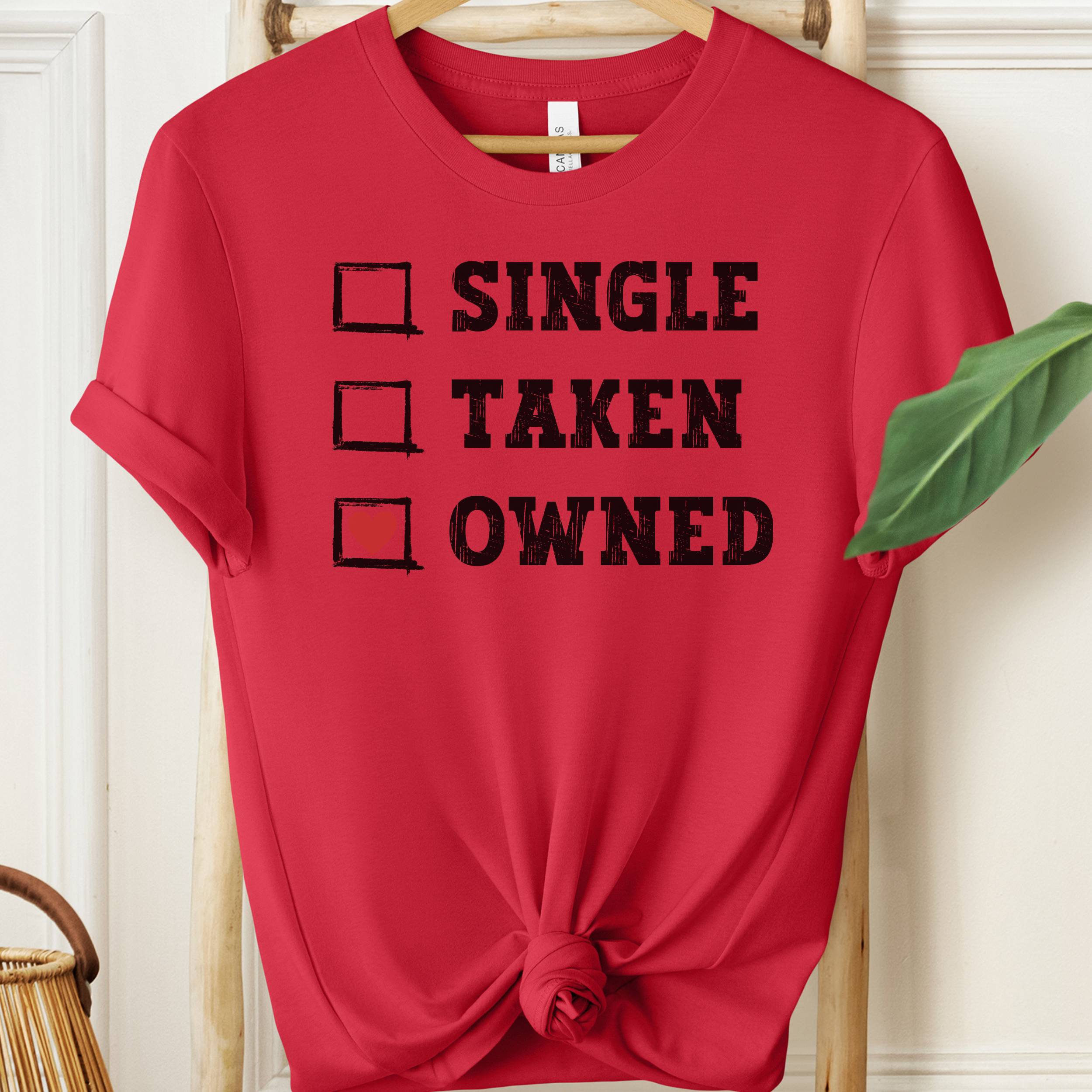 Red t-shirt with text 'Single, Taken, Owned' on a hanger.
