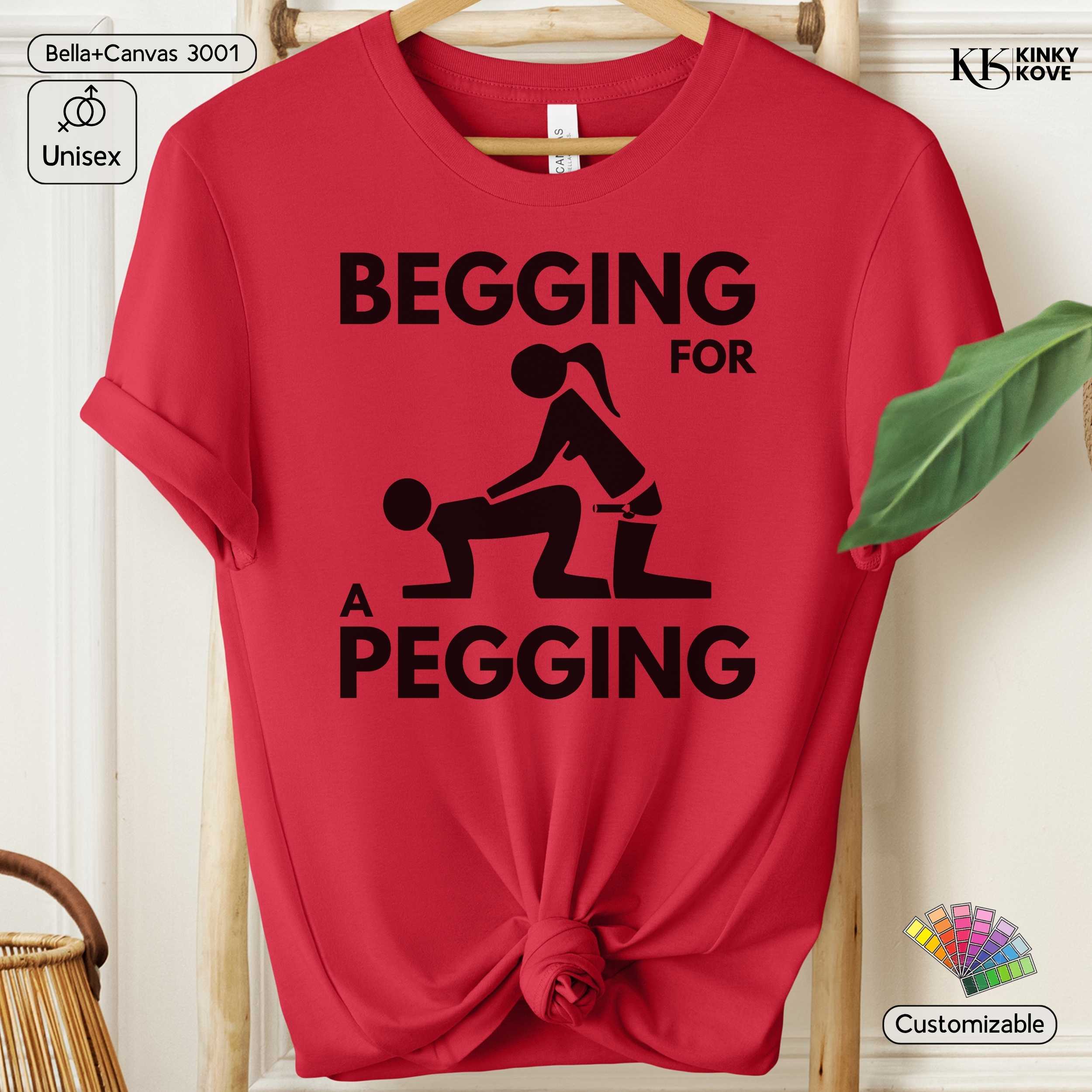 Red t-shirt with black graphic and text 'Begging for a Pegging' on a hanger.