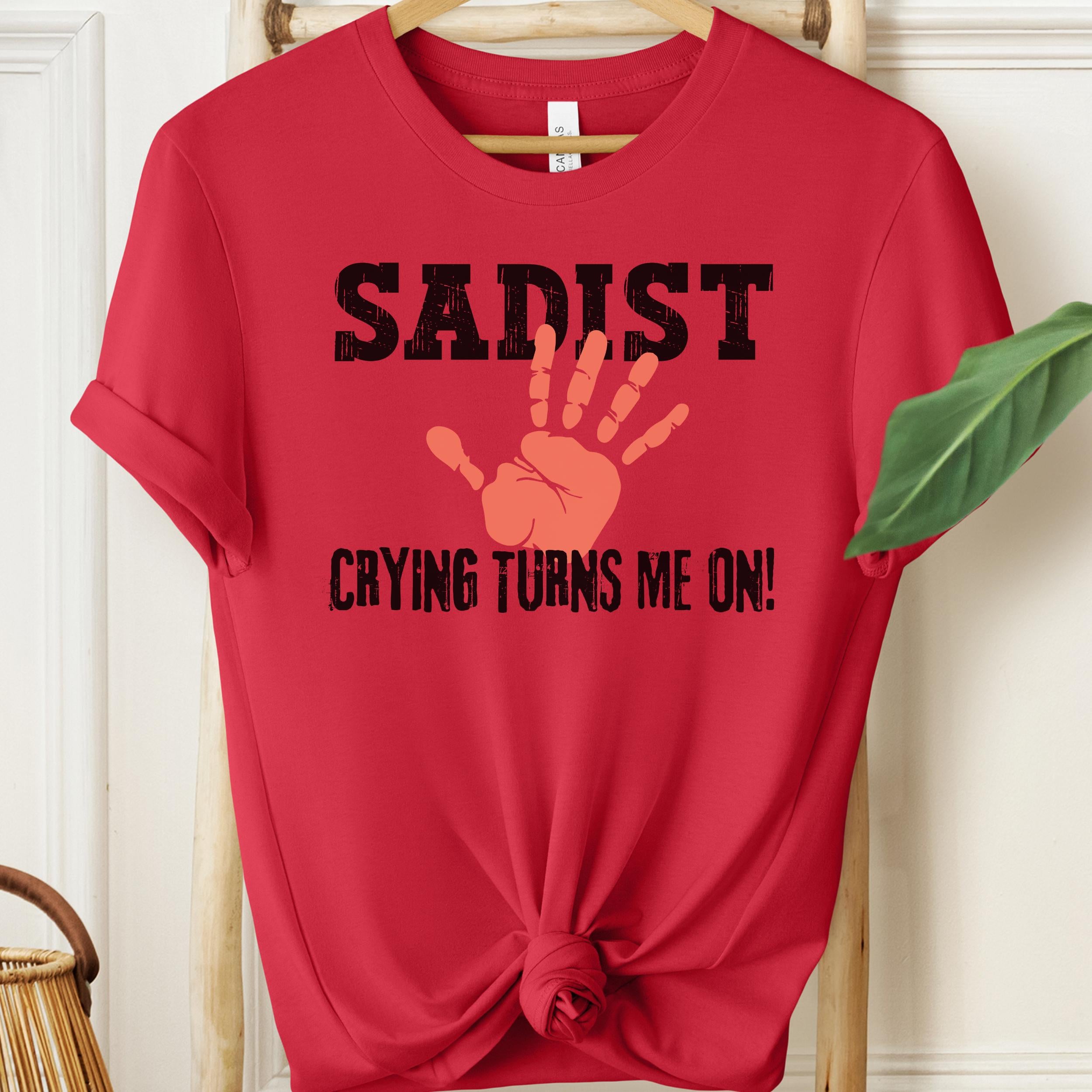 Red unisex t-shirt featuring bold “Sadist – Crying Turns Me On” text with orange handprint graphic