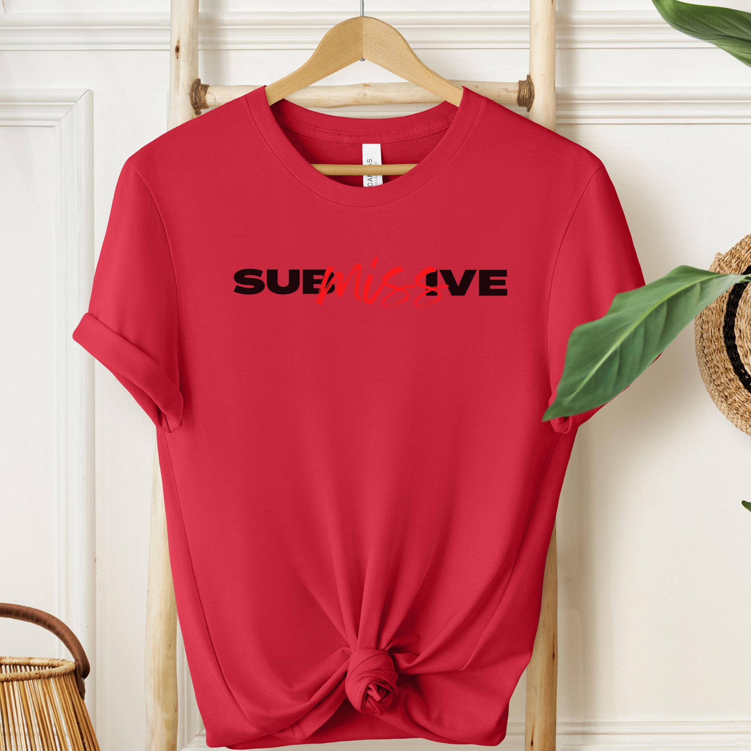 Red t-shirt with 'SUBMISSIVE' text on a wooden hanger against a white wall.