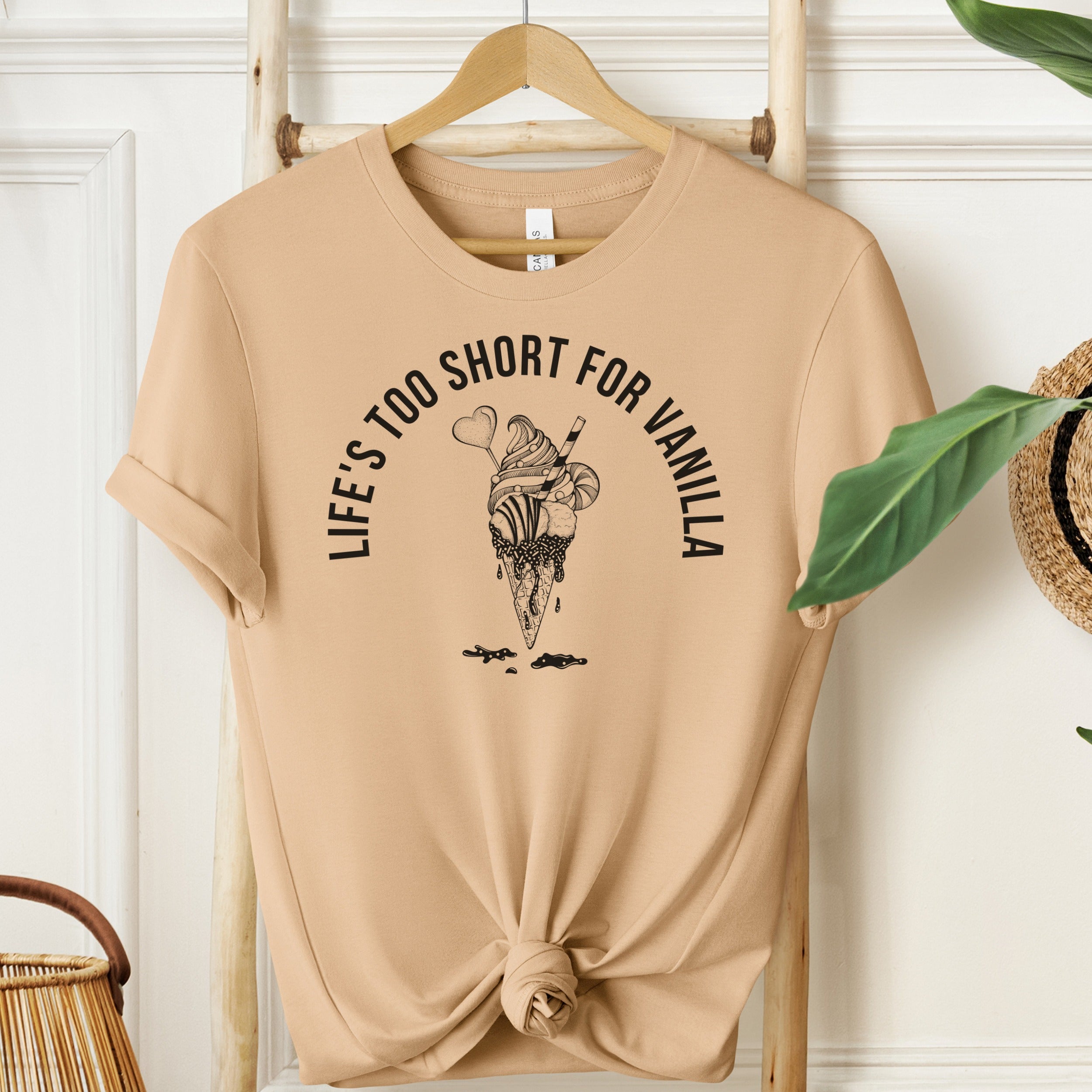 Beige t-shirt with ice cream graphic and text on a hanger against a white wall.
