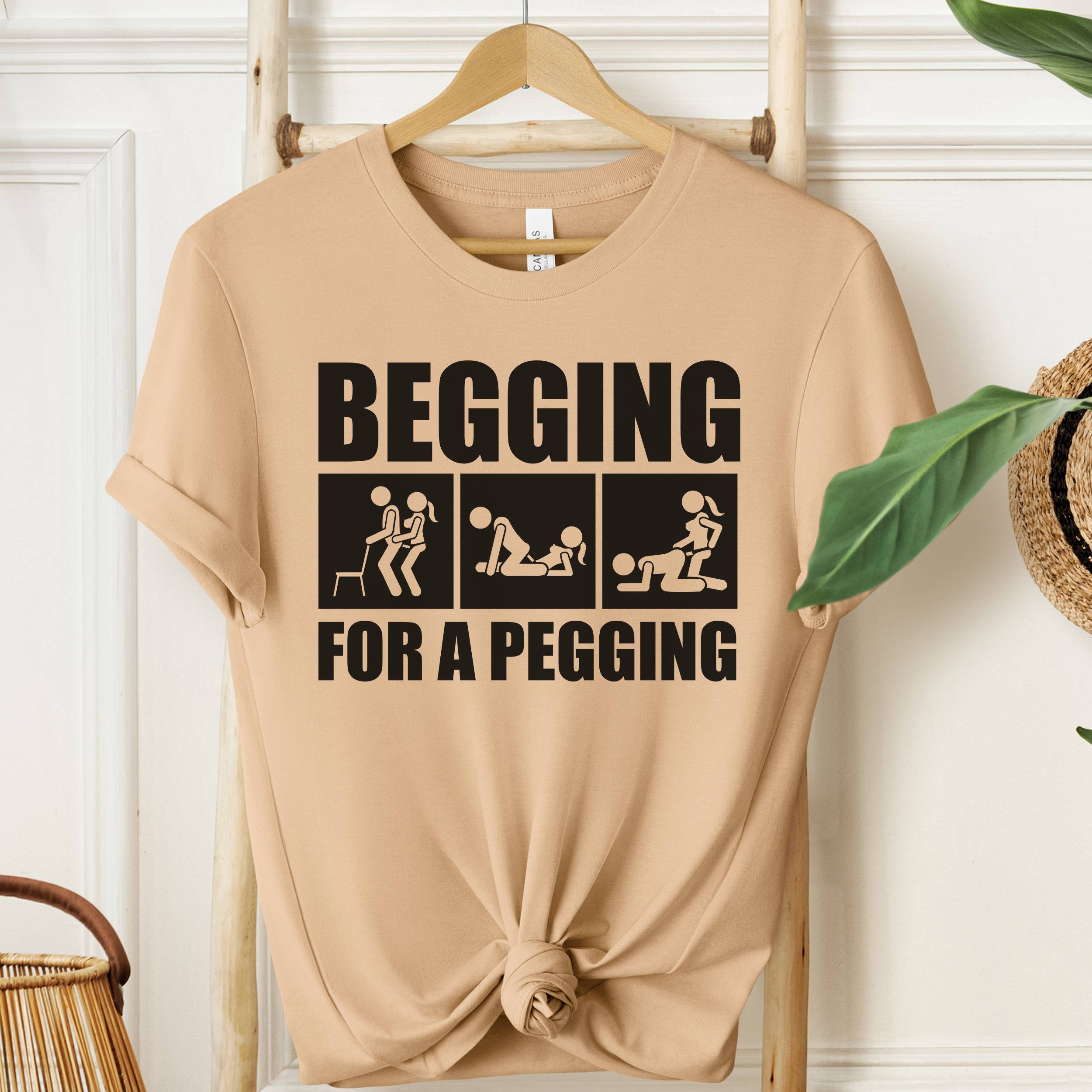 Beige t-shirt with graphic text on a wooden hanger against a white wall.