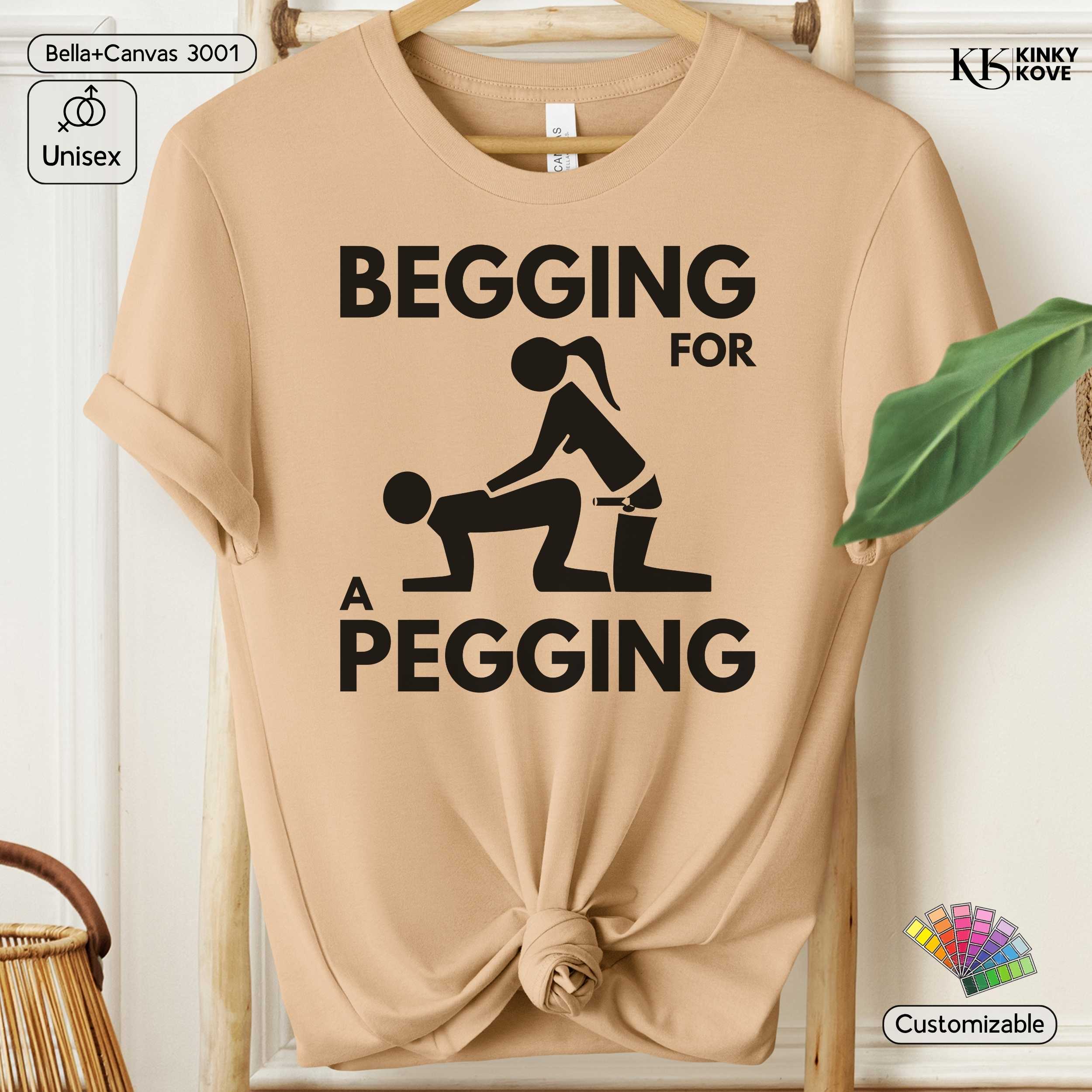 Beige t-shirt with graphic design and text 'Begging for a Pegging' on a hanger.