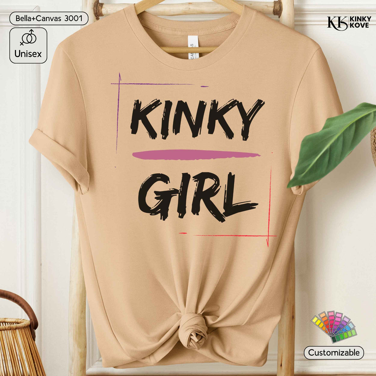 A beige short-sleeve t-shirt with a knotted hem, featuring the text 'KINKY GIRL' in black brush-style lettering with a pink horizontal stripe accent. The shirt is displayed on a wooden hanger against a white paneled wall background.